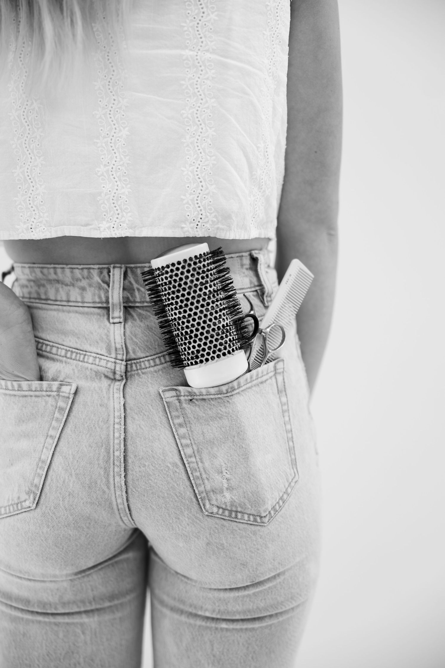 Black and white photo of a hairstylist with hair brush and scissors tucked into back pocket of jeans.