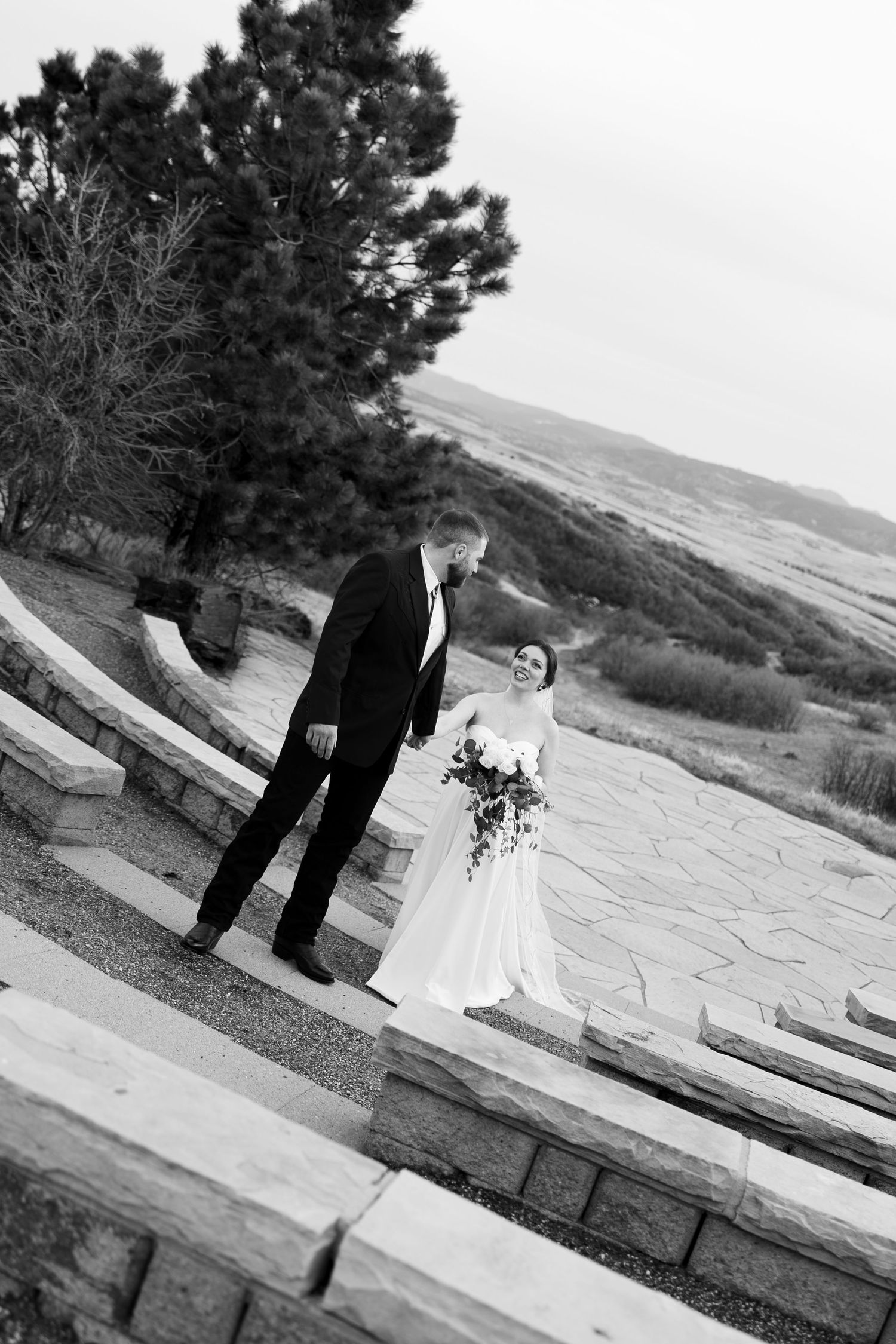 Black and white photo of bride and groom sharing a tender moment on stone steps at outdoor venue.