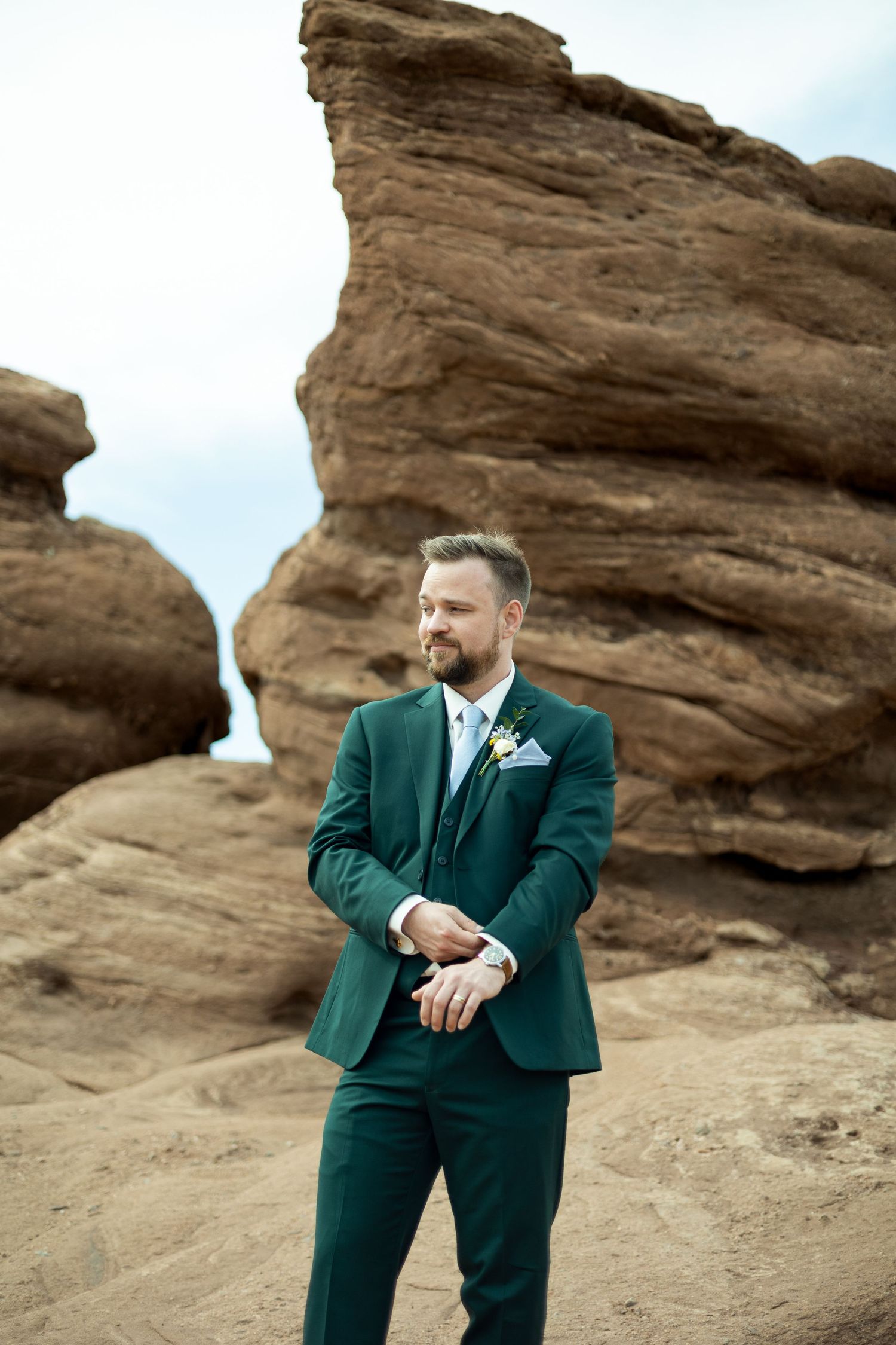 Person in emerald green suit poses against dramatic red rock formations in desert landscape.