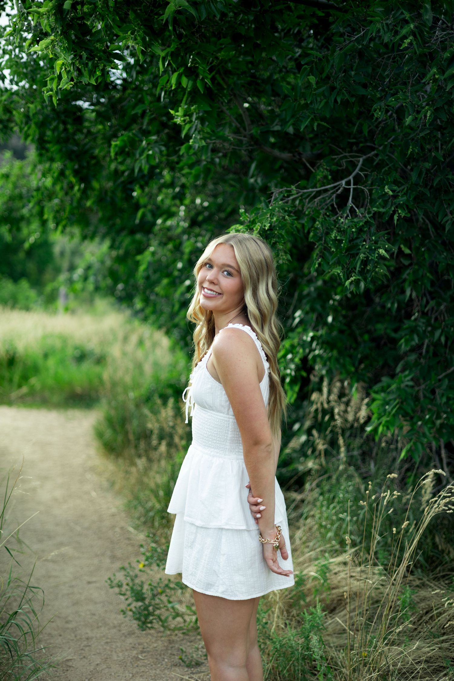 A series of outdoor portrait photos showing someone in a white sundress posing against lush green foliage along a nature path.