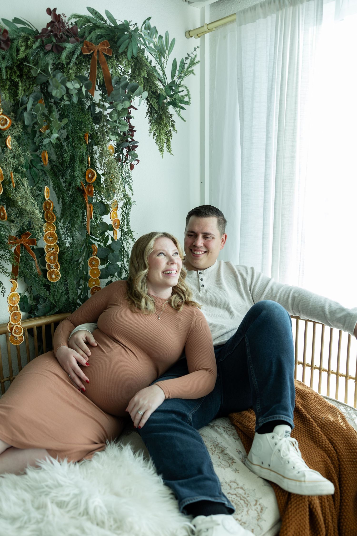 A couple relaxes together on a white fluffy rug with decorative plants and orange accents in the background.