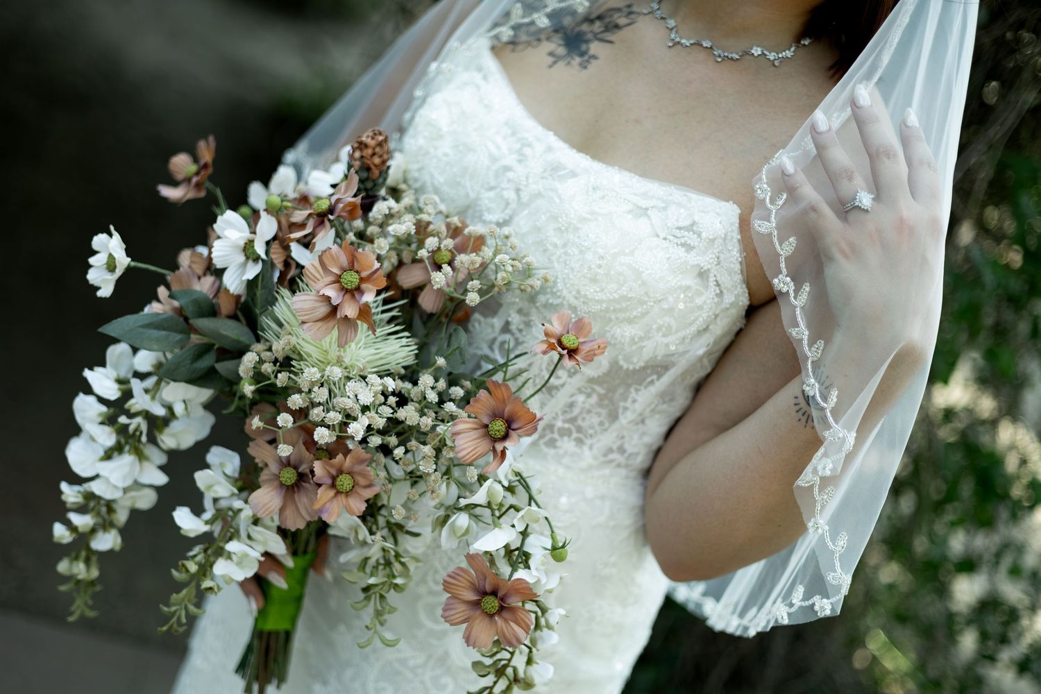 Bride in white lace wedding dress holding a rustic bouquet of wildflowers and baby's breath outdoors.