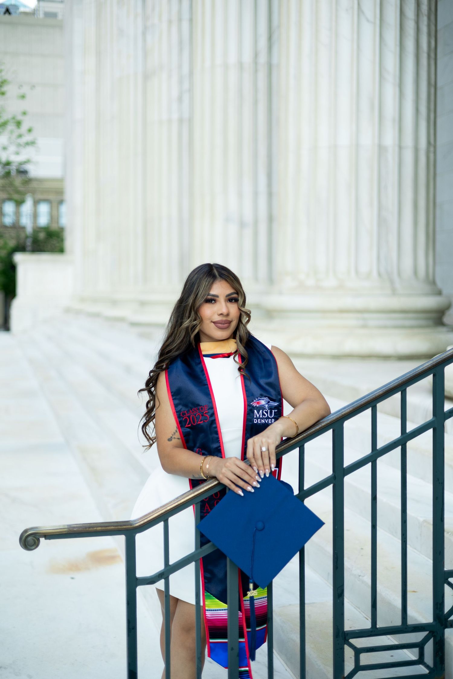Graduate in MSU Dental graduation stole poses with blue cap beside classical white columns.