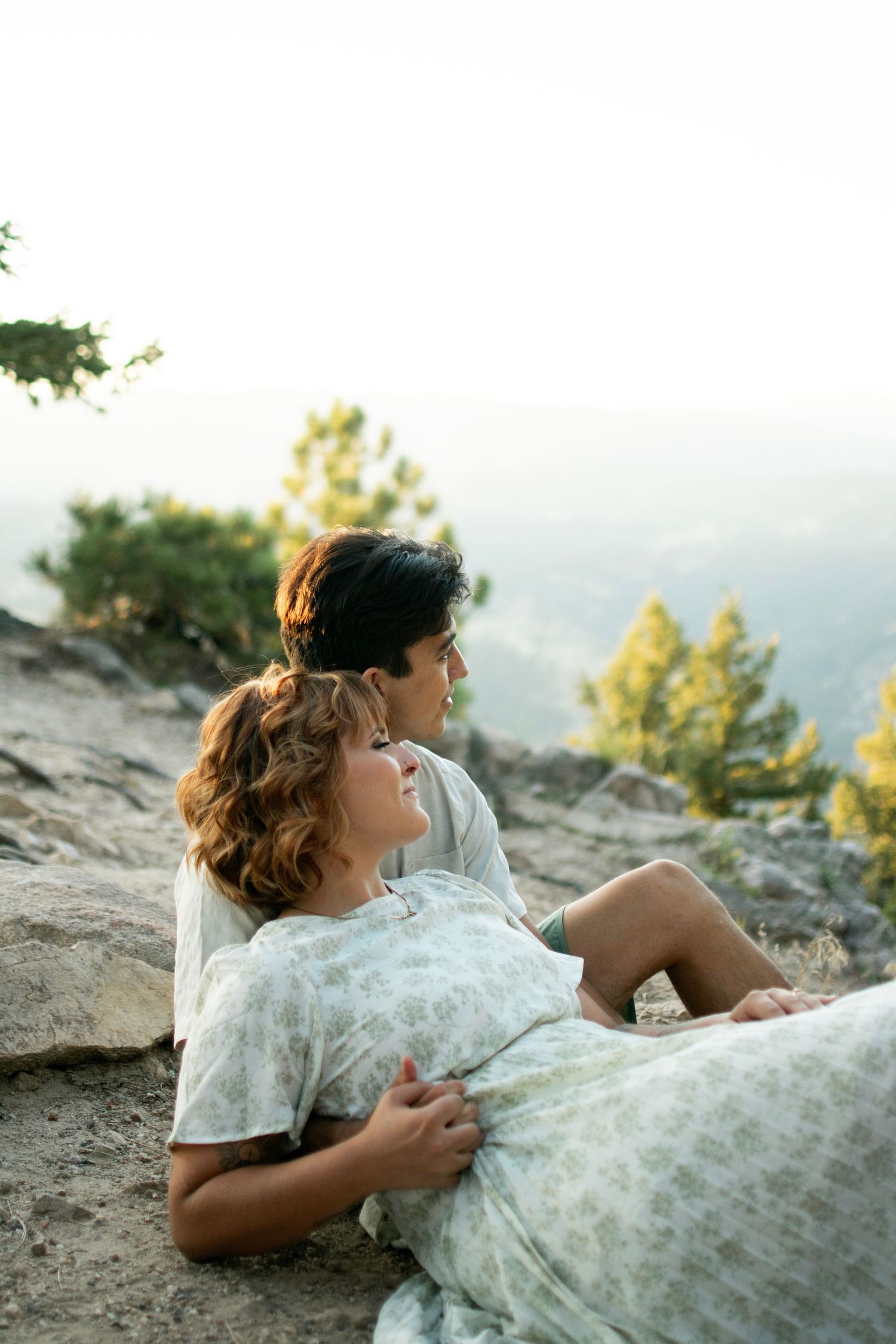 A couple relaxes on rocky terrain while taking in mountain views at sunset.