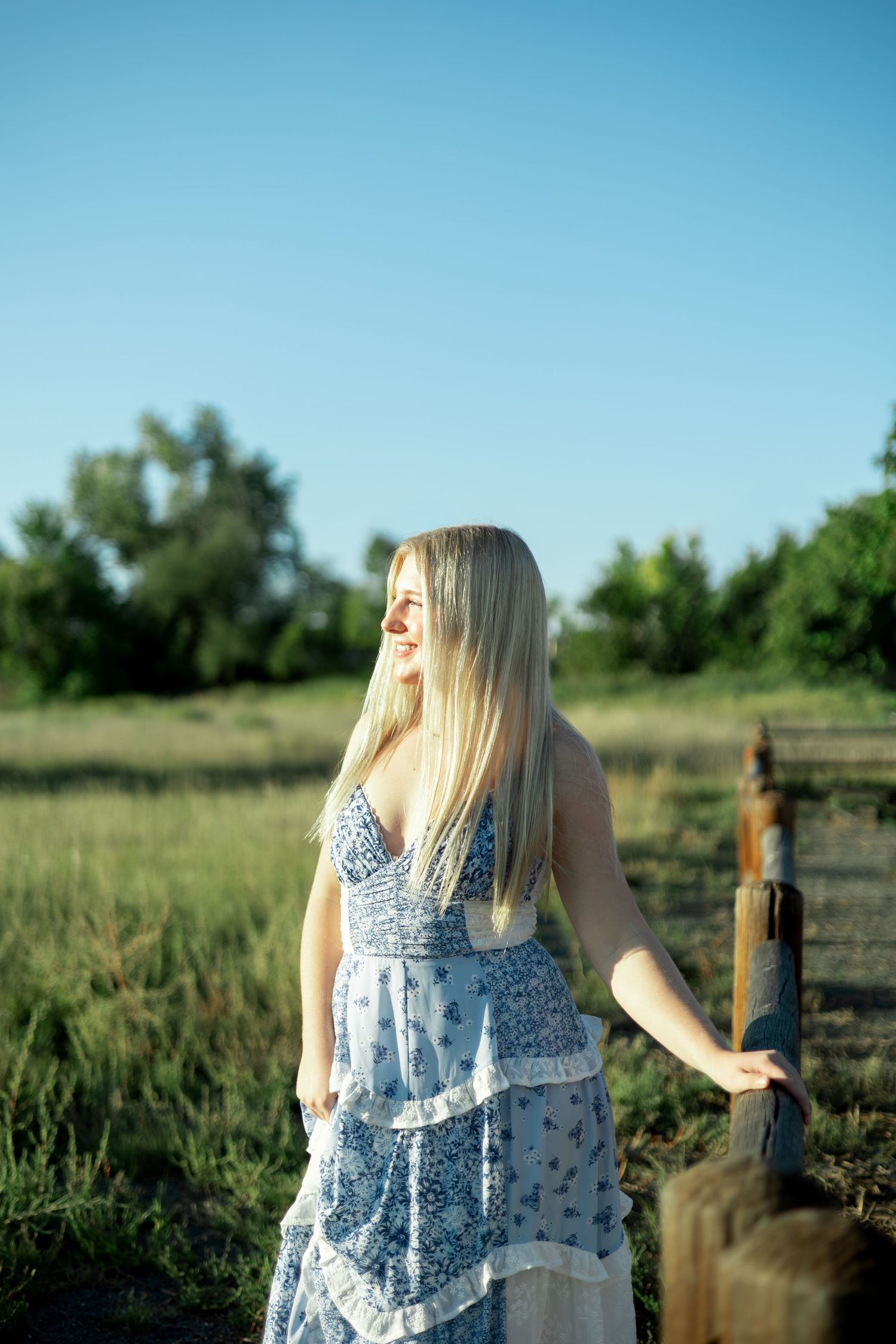 A person in a white floral sundress stands in a grassy field on a sunny summer day.