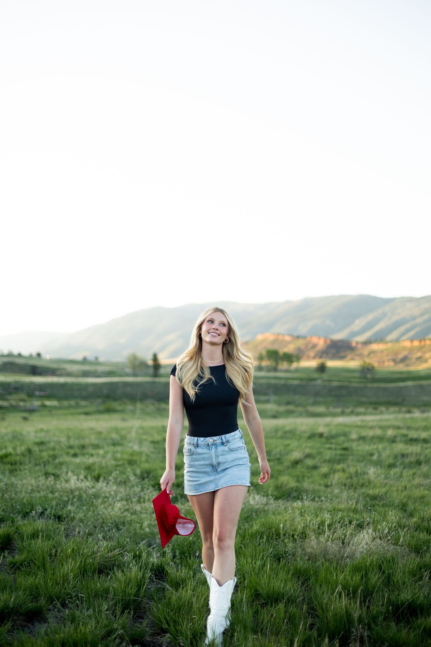Casual summer style with white boots and denim against a scenic mountain landscape at sunset.