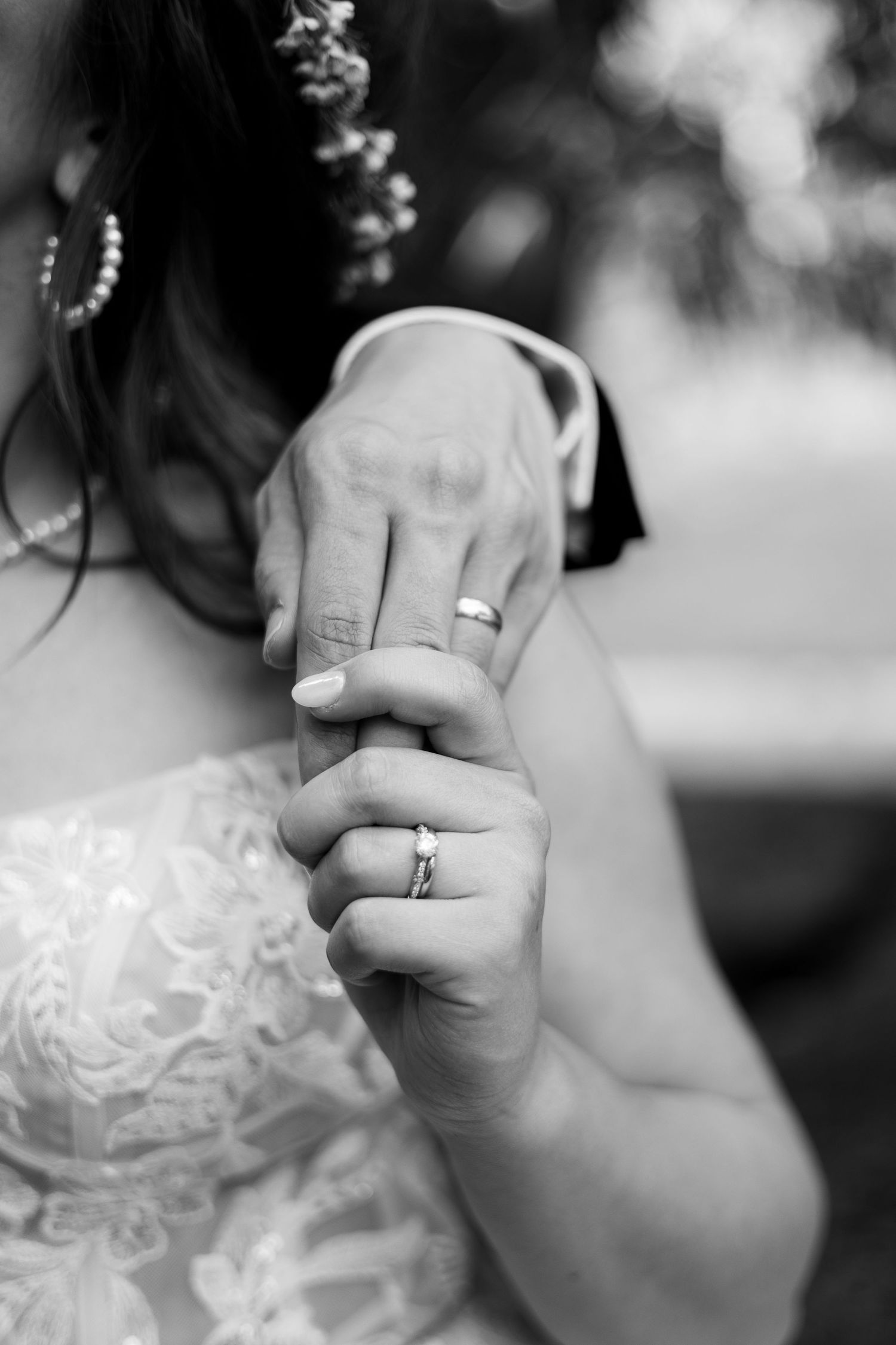 Black and white close-up of wedding rings and joined hands.