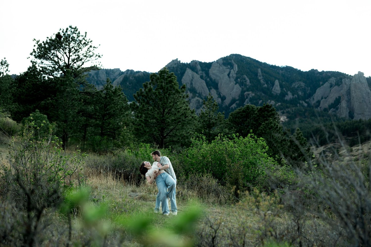 Couple embracing in a meadow with the Flatirons mountain range in Boulder, Colorado in the background.