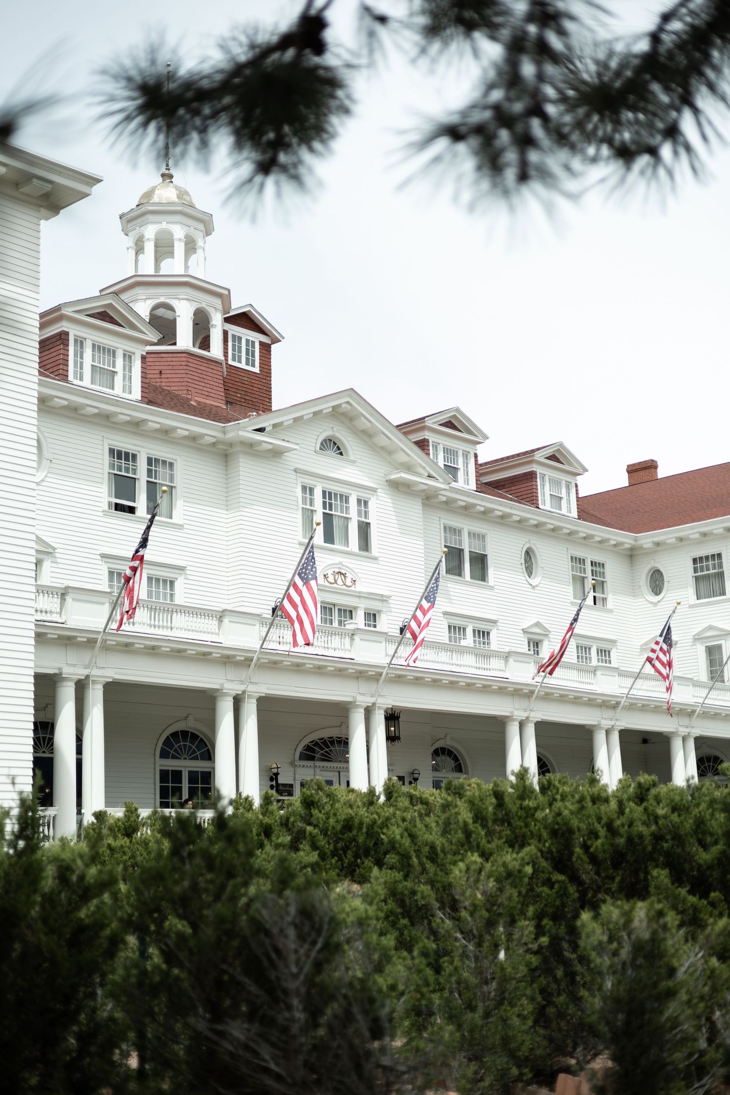 White colonial style hotel building with American flags and green hedges along the front exterior.