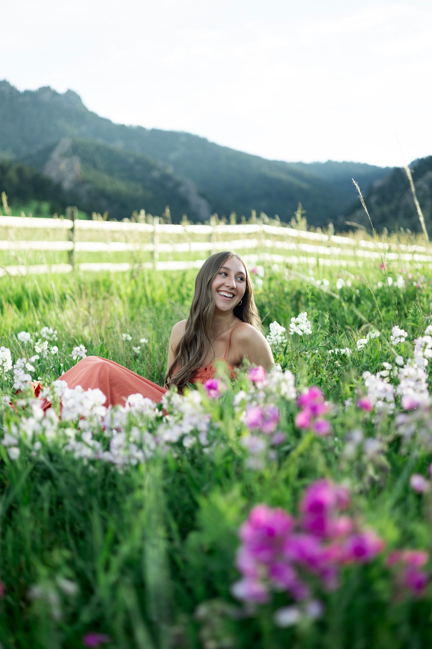 Person lying in a green meadow surrounded by vibrant pink wildflowers with mountains in the background.