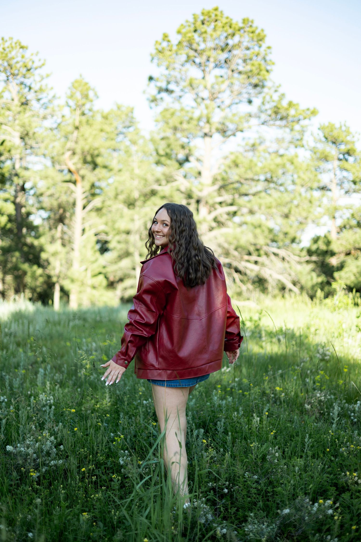 A person in a burgundy sweater twirling joyfully in a sunlit meadow filled with tall grass and wildflowers.