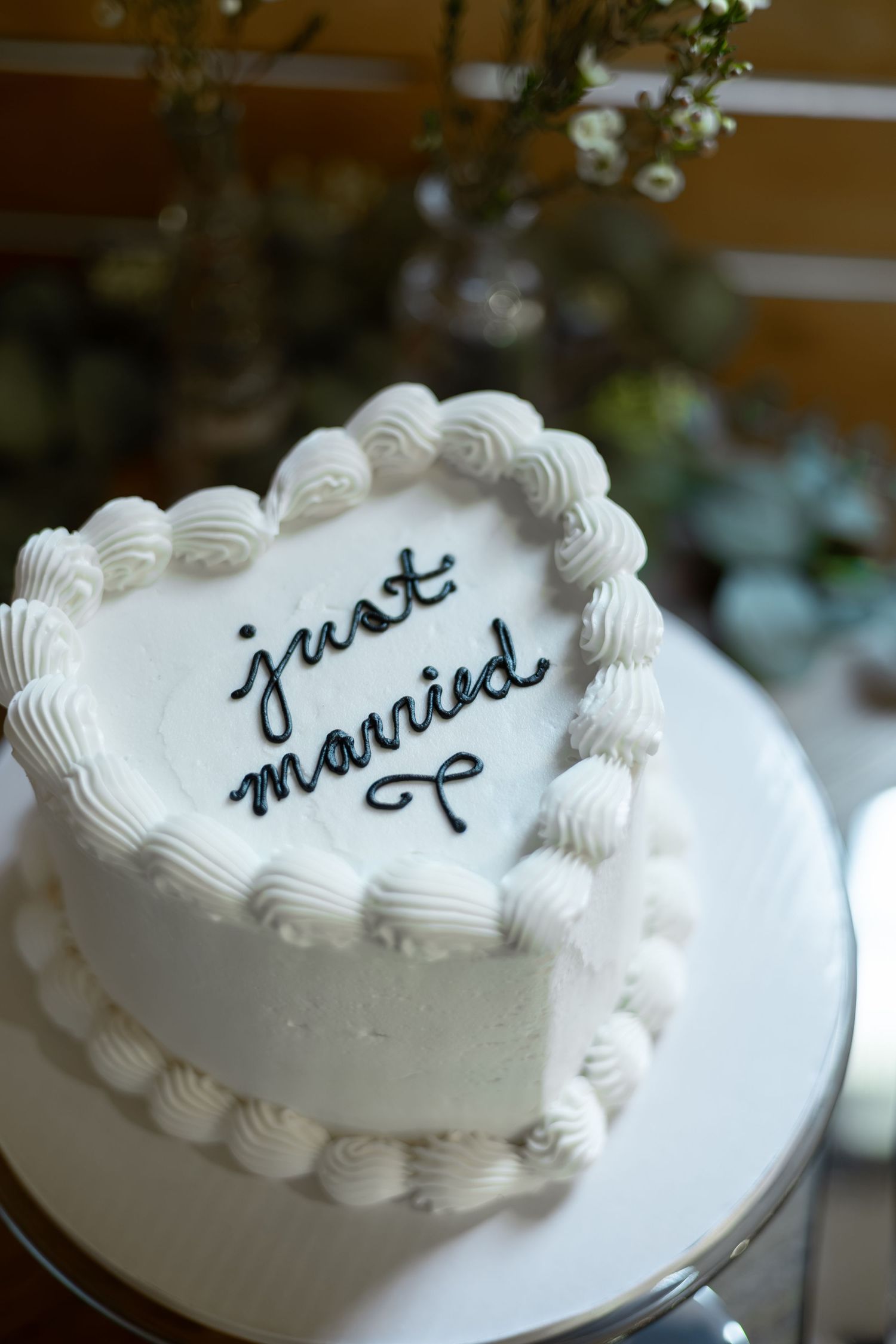 White heart-shaped wedding cake decorated with rosettes and cursive just married inscription on a white cake stand.
