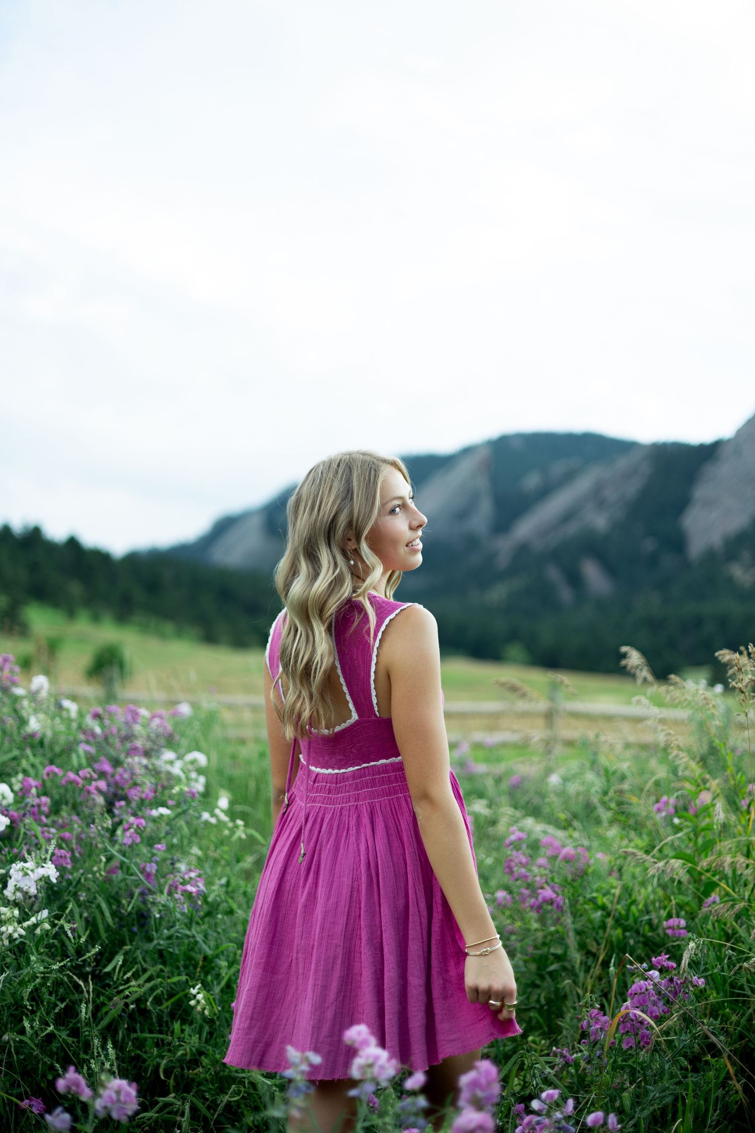 Figure in magenta dress stands among wildflowers with mountain vista in the background.