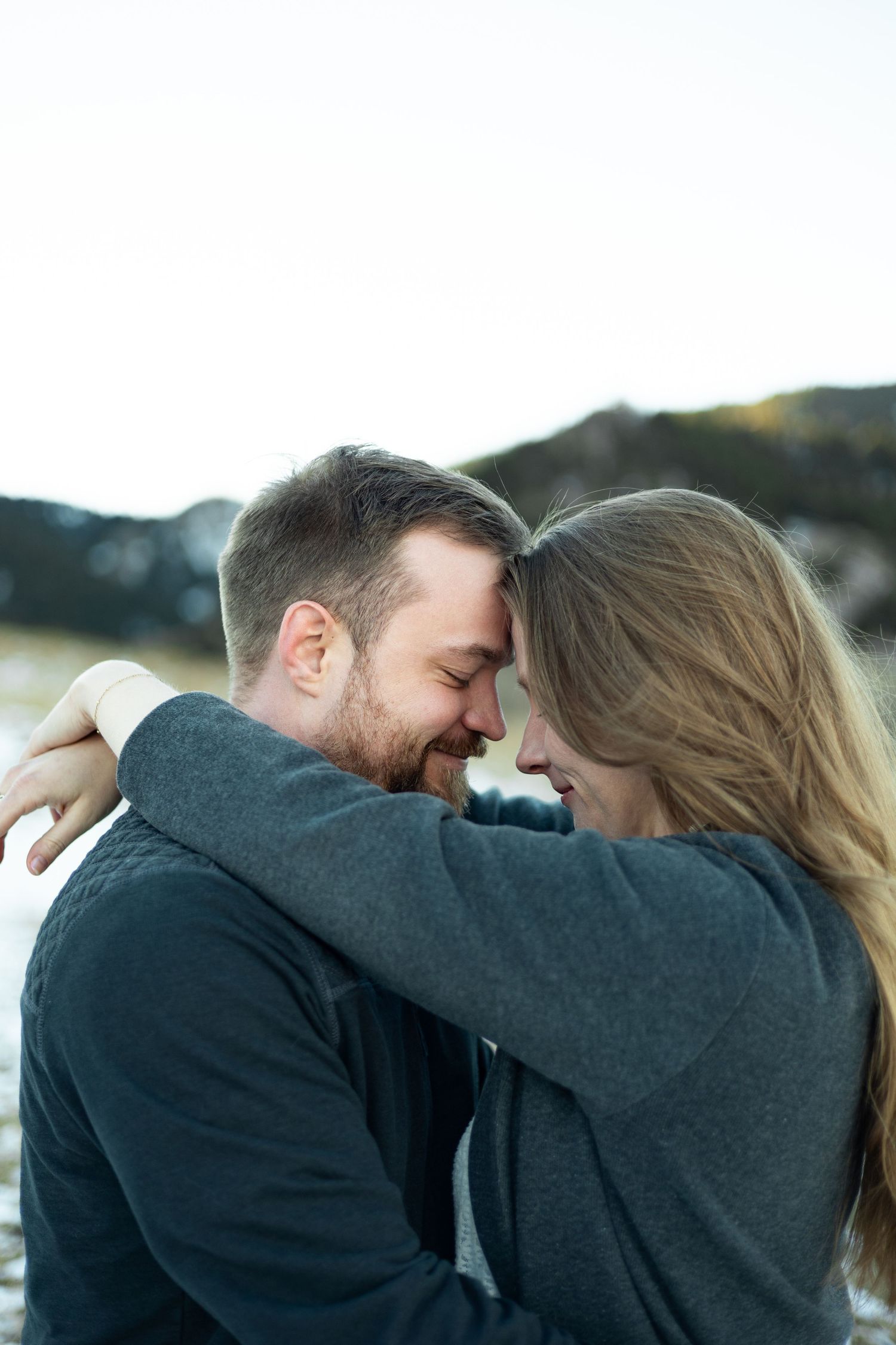 An intimate moment shared between a couple wearing dark sweaters against a mountain backdrop.