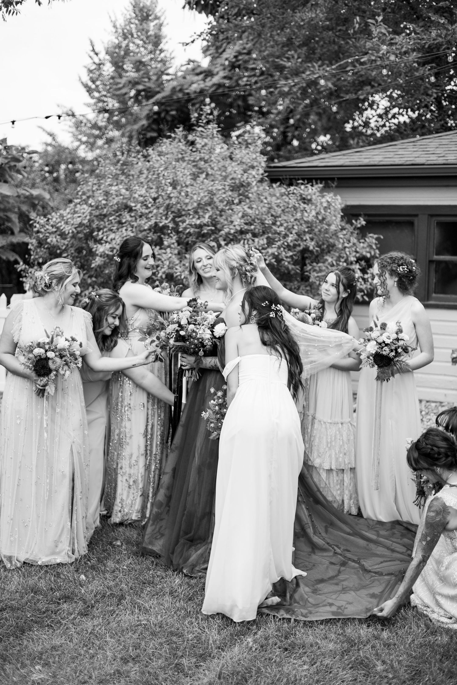 Black and white photo of bridal party in flowing dresses sharing a joyful moment.
