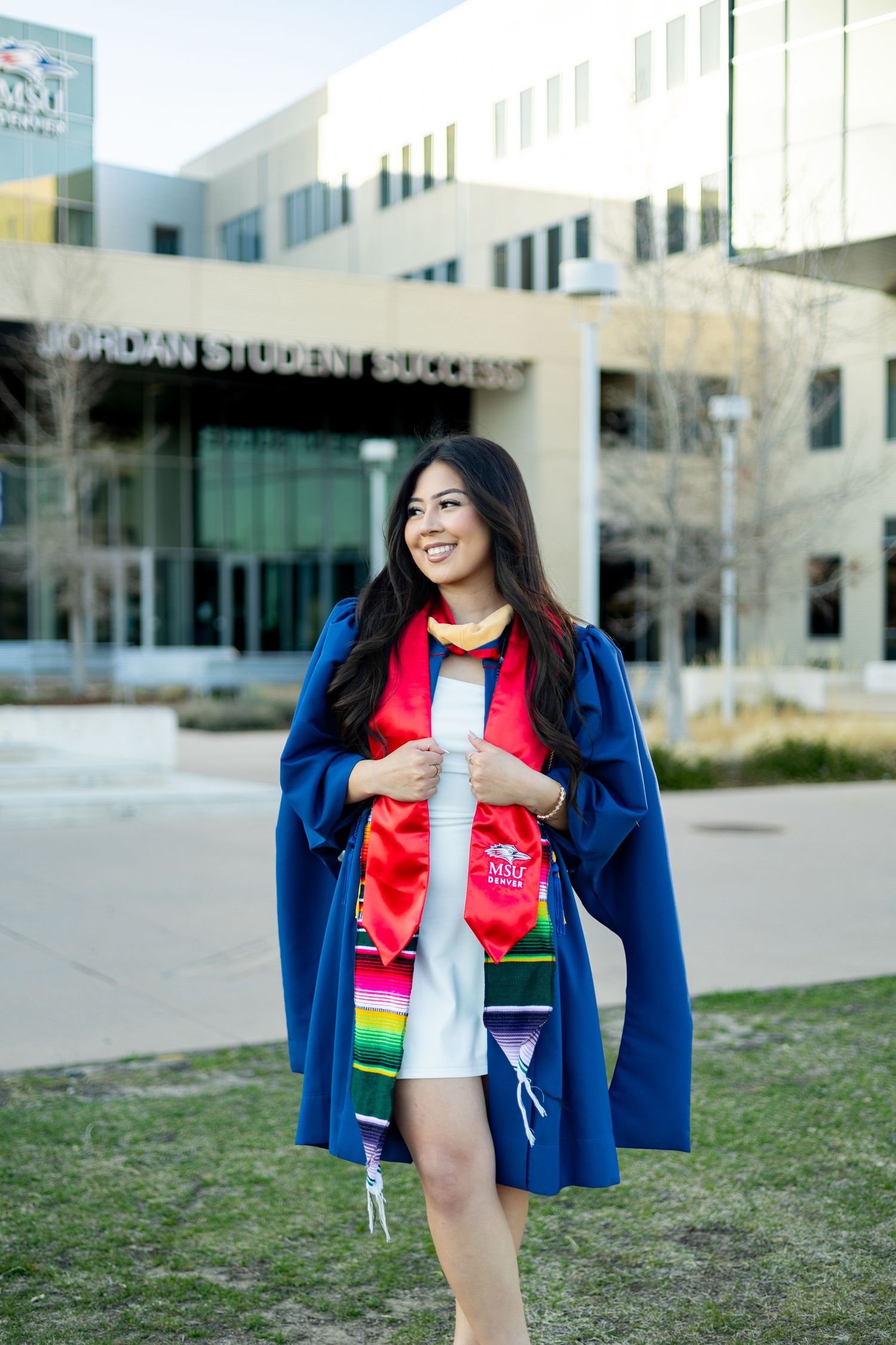 Graduate posing outside a modern university building wearing blue jacket and red shirt in a series of celebratory photos.