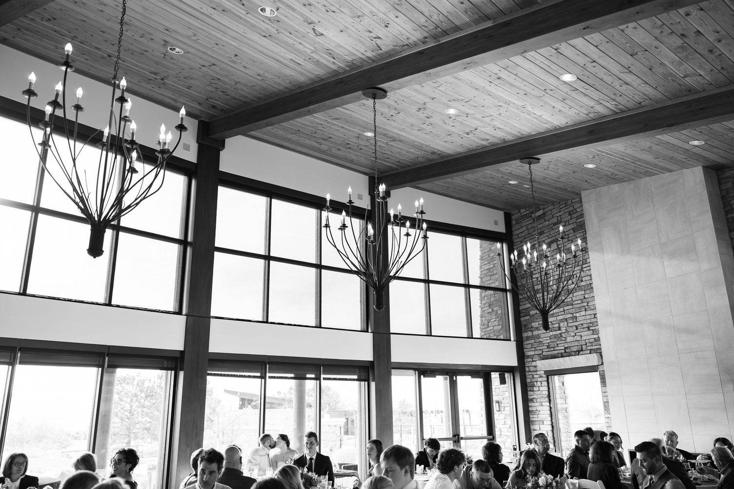 Black and white photo of elegant wedding reception venue with high ceilings, chandeliers, and large windows.