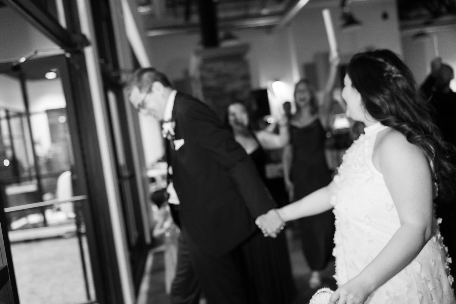 Black and white photo of a bride and groom holding hands entering their wedding reception.