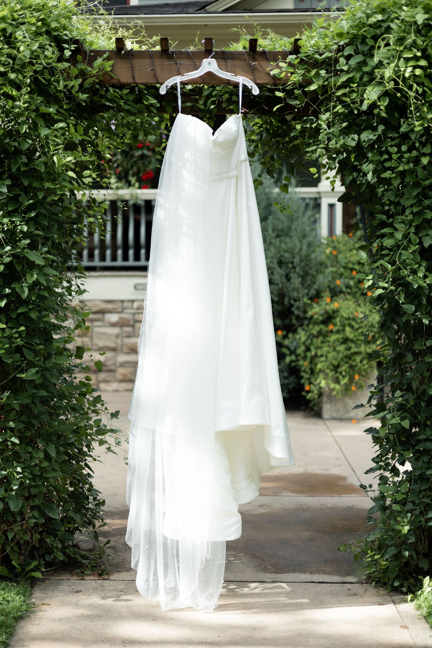 White wedding dress hangs between green garden archways.