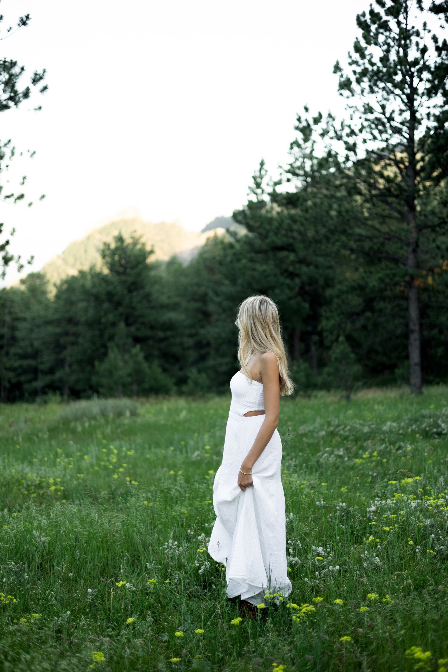 Artistic sequence showing movement in a flowing white dress against a natural backdrop of trees and meadow flowers.