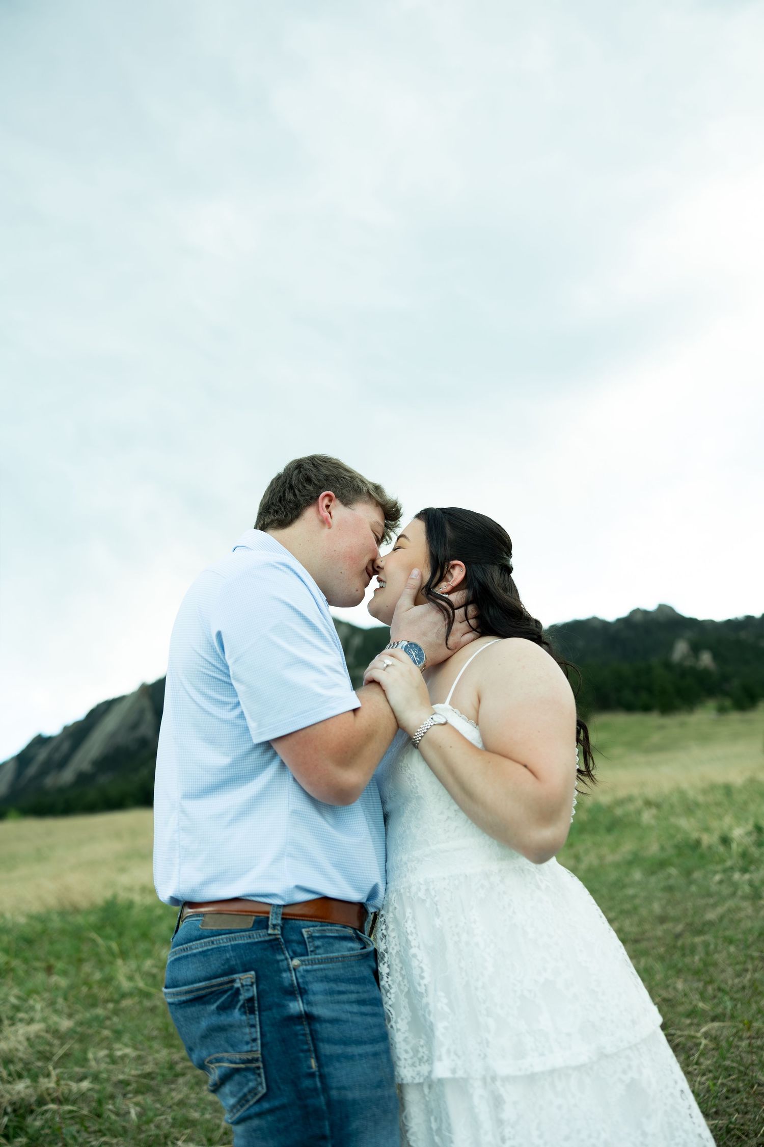 Couple sharing a romantic moment in a field with the Flatirons mountains in the background.