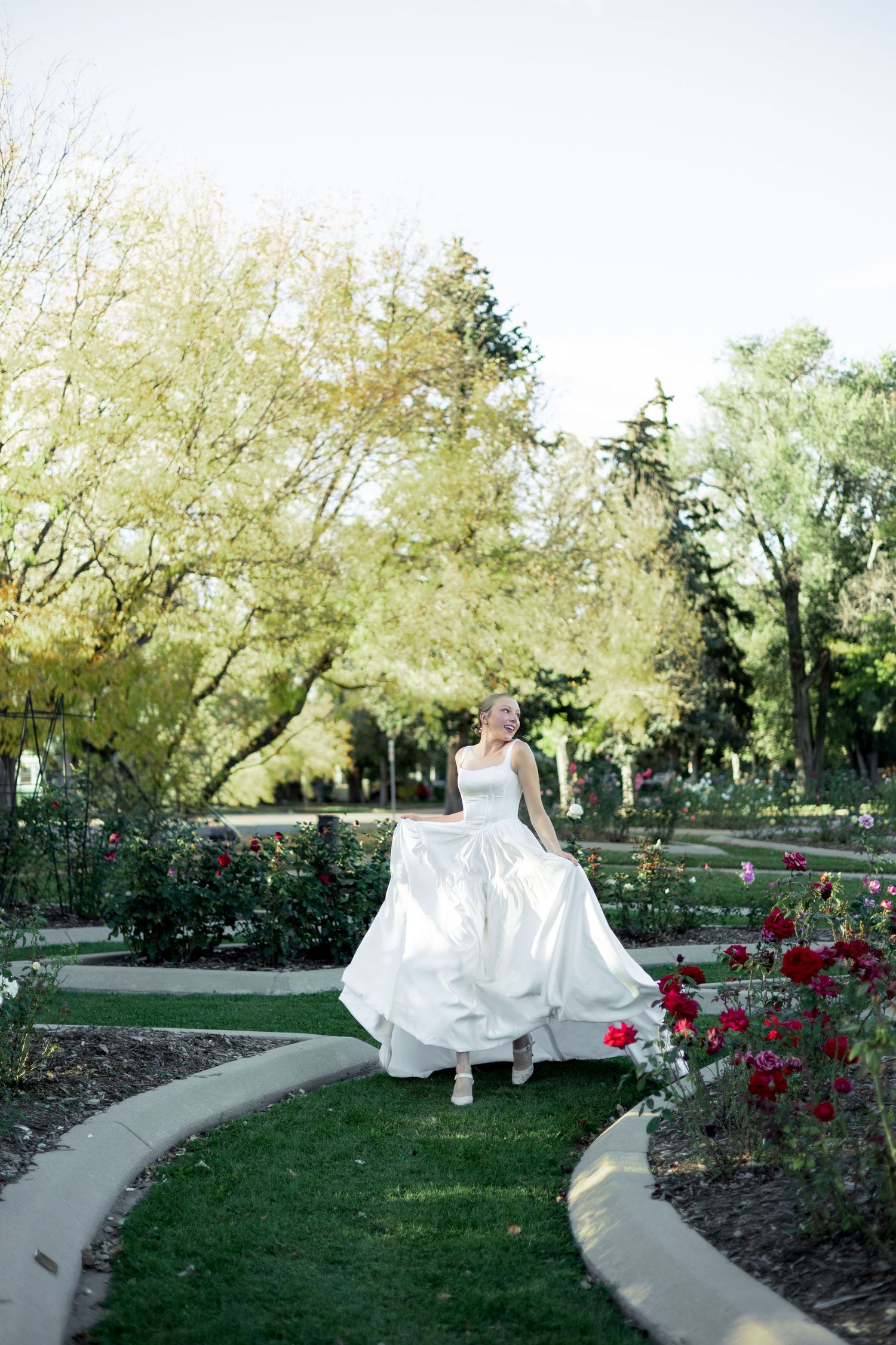 A winding garden path leads through blooming red roses and green trees in a serene outdoor setting.