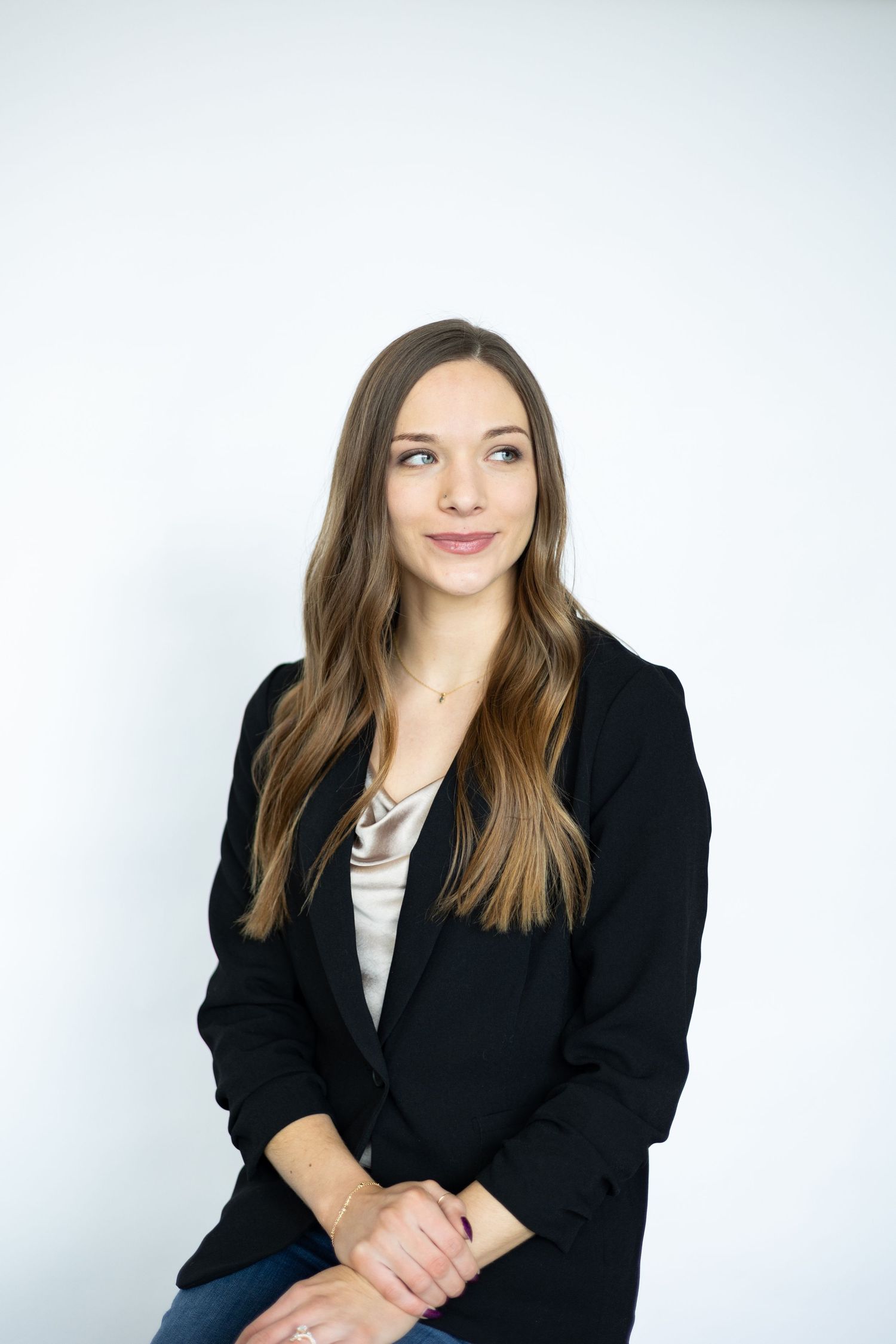 Professional headshot of someone in a black blazer and neutral top against white background.