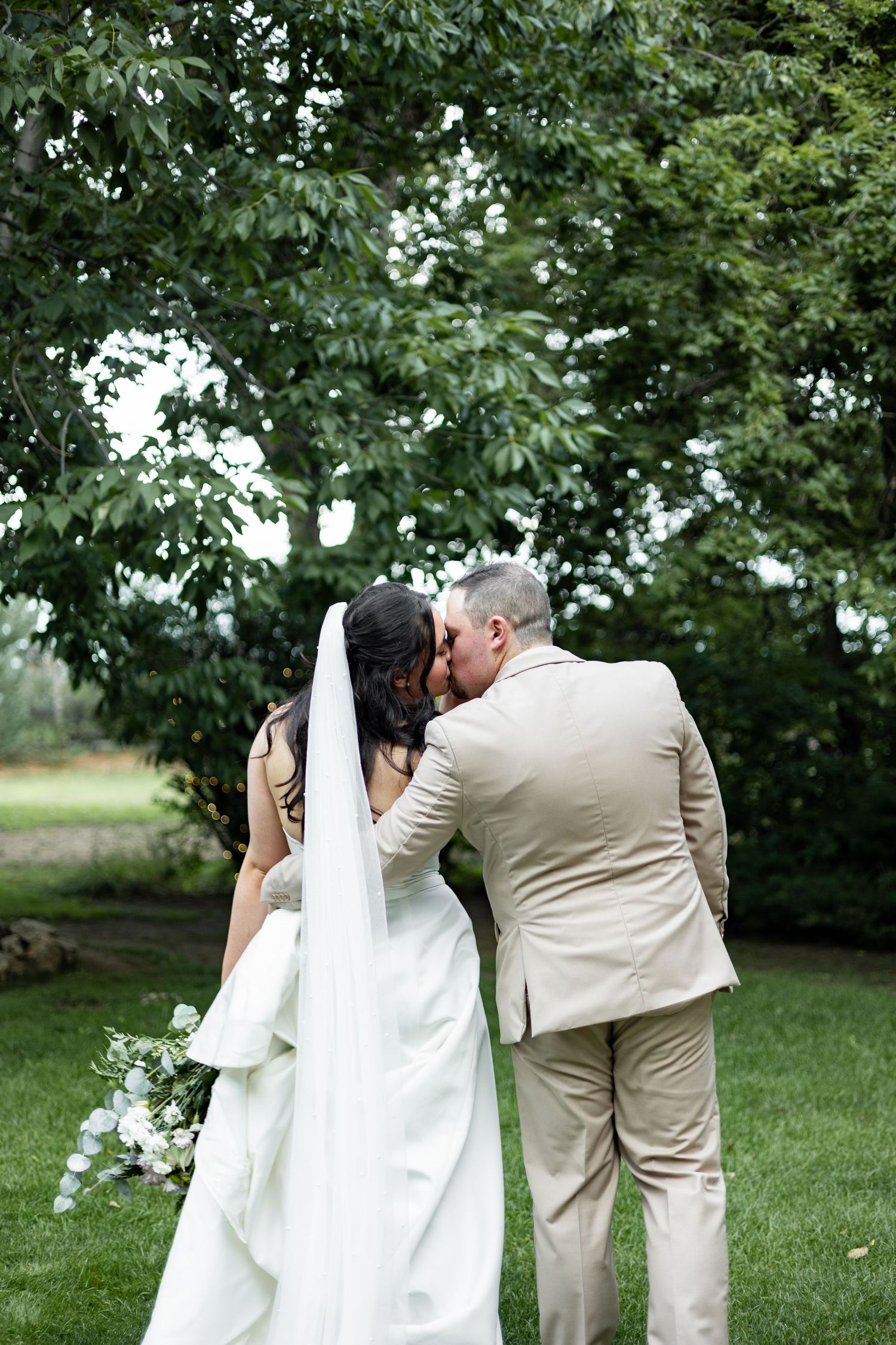 Intimate wedding couple moment captured from behind against a backdrop of lush green trees.