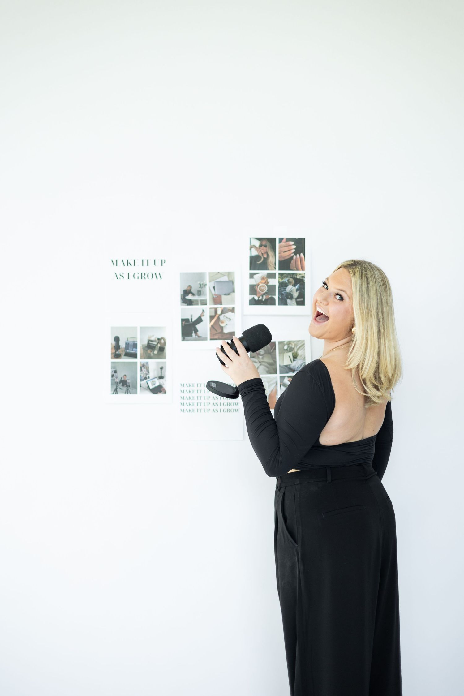 Person in black dress holding microphone against wall with photo display.