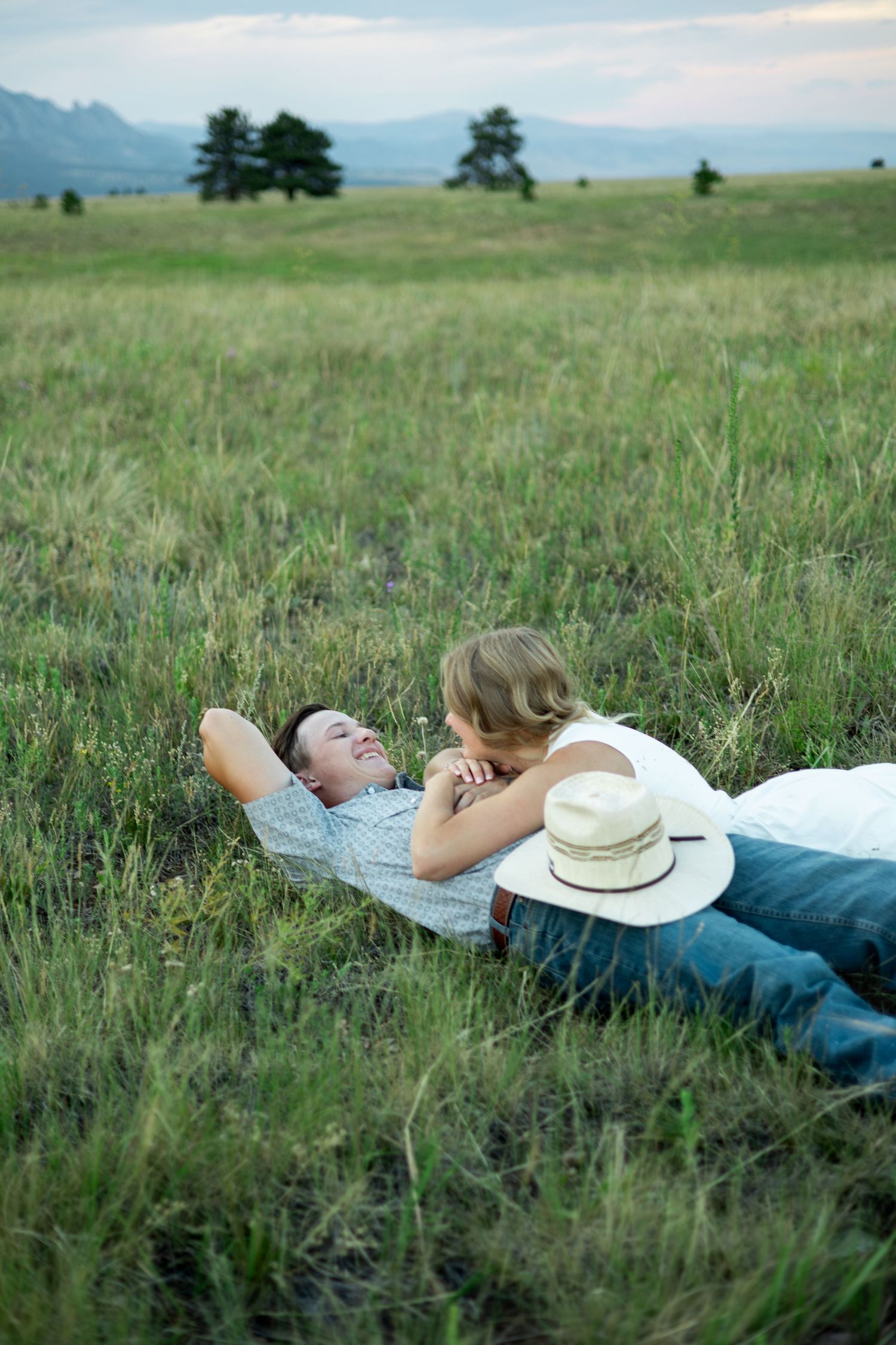 Couple relaxing together on a blanket in a grassy meadow with mountains and trees in the background.