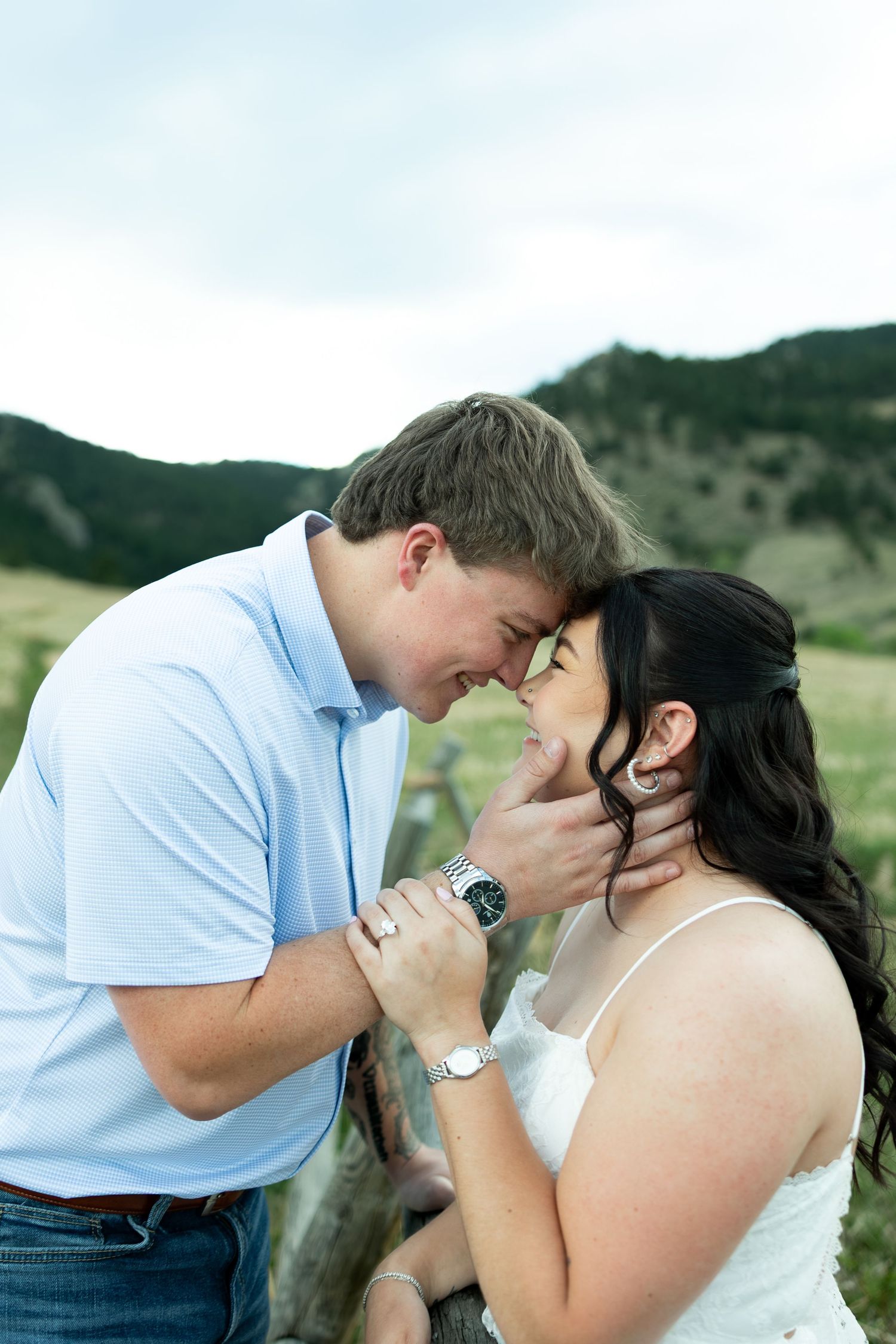 Couple sharing a romantic forehead touch outdoors with mountain landscape backdrop, man gently holding womans face.
