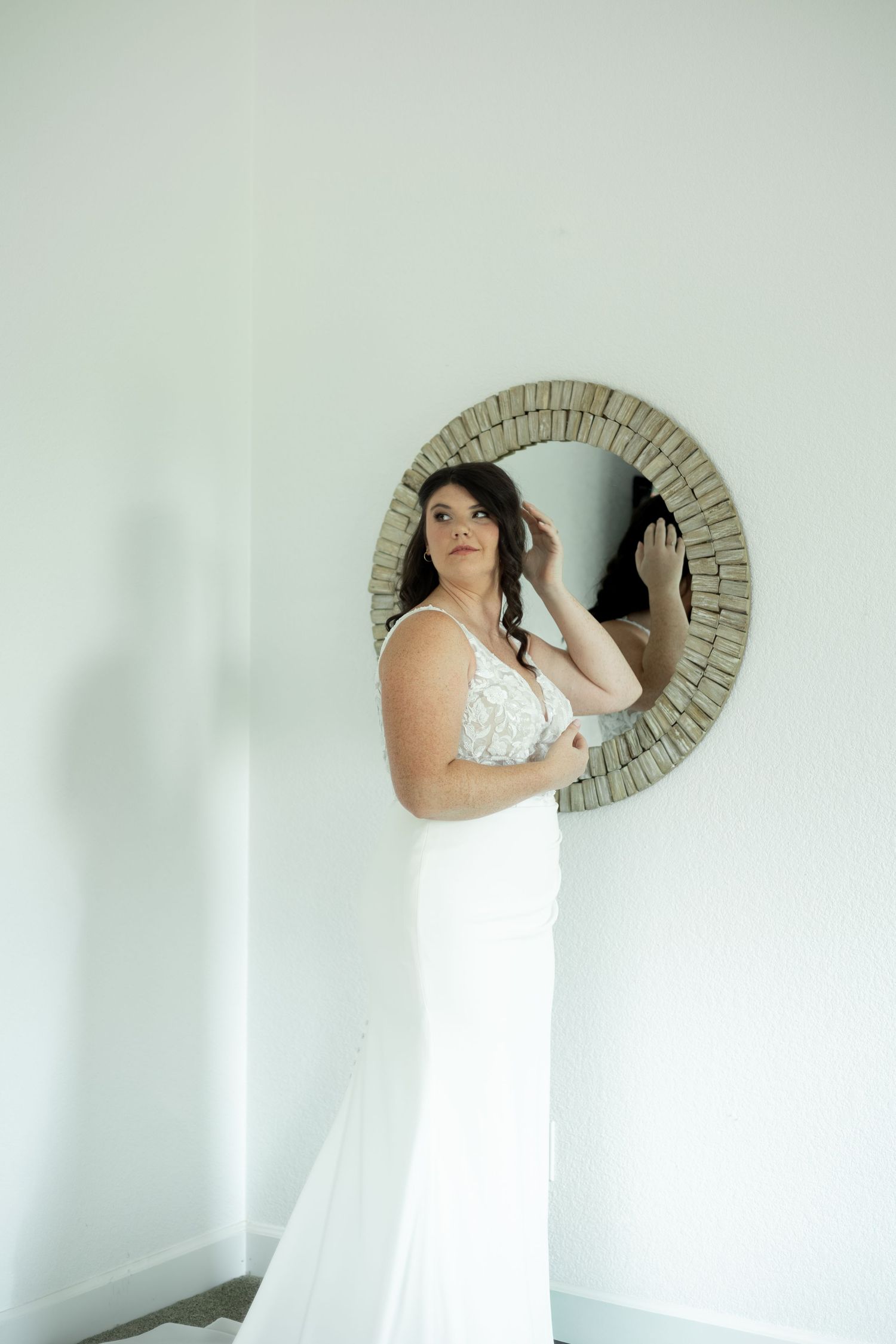 A figure in a white dress poses artistically with a circular mirror against a minimalist white wall.