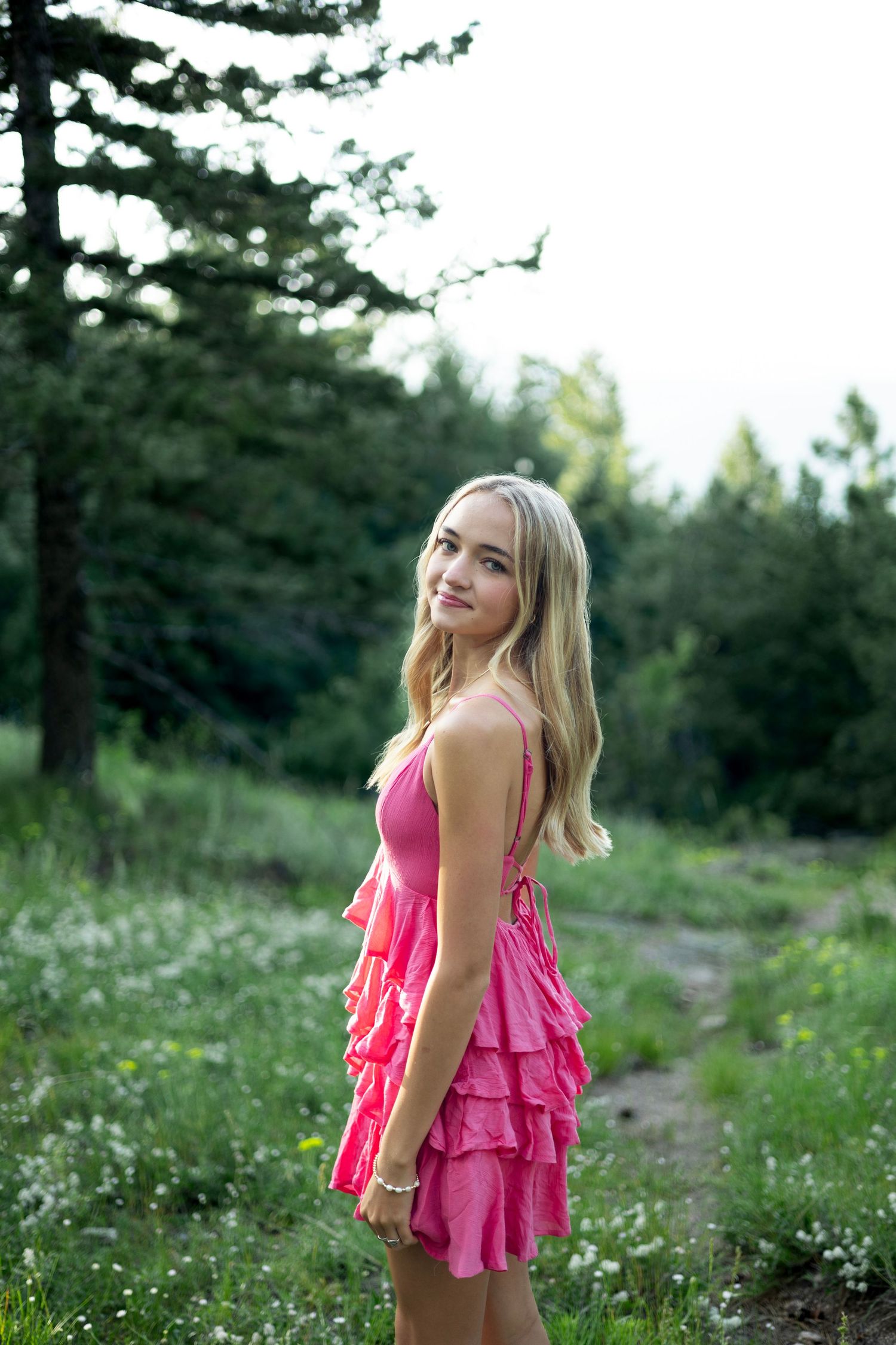 Pink ruffled sundress stands out against the forest backdrop on a summer evening.
