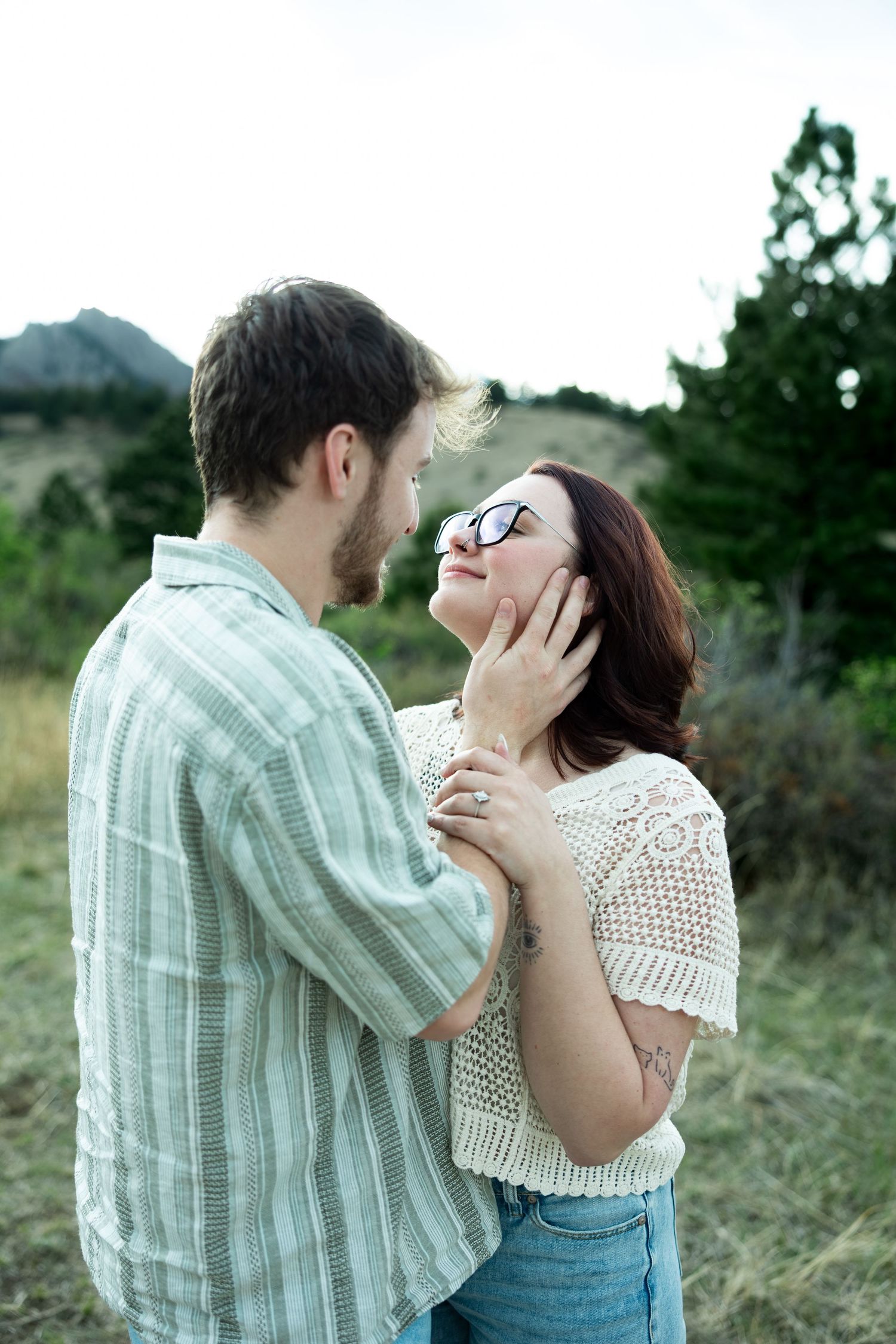 Couple sharing a romantic moment outdoors, man gently holding woman's face near rocky mountain landscape.