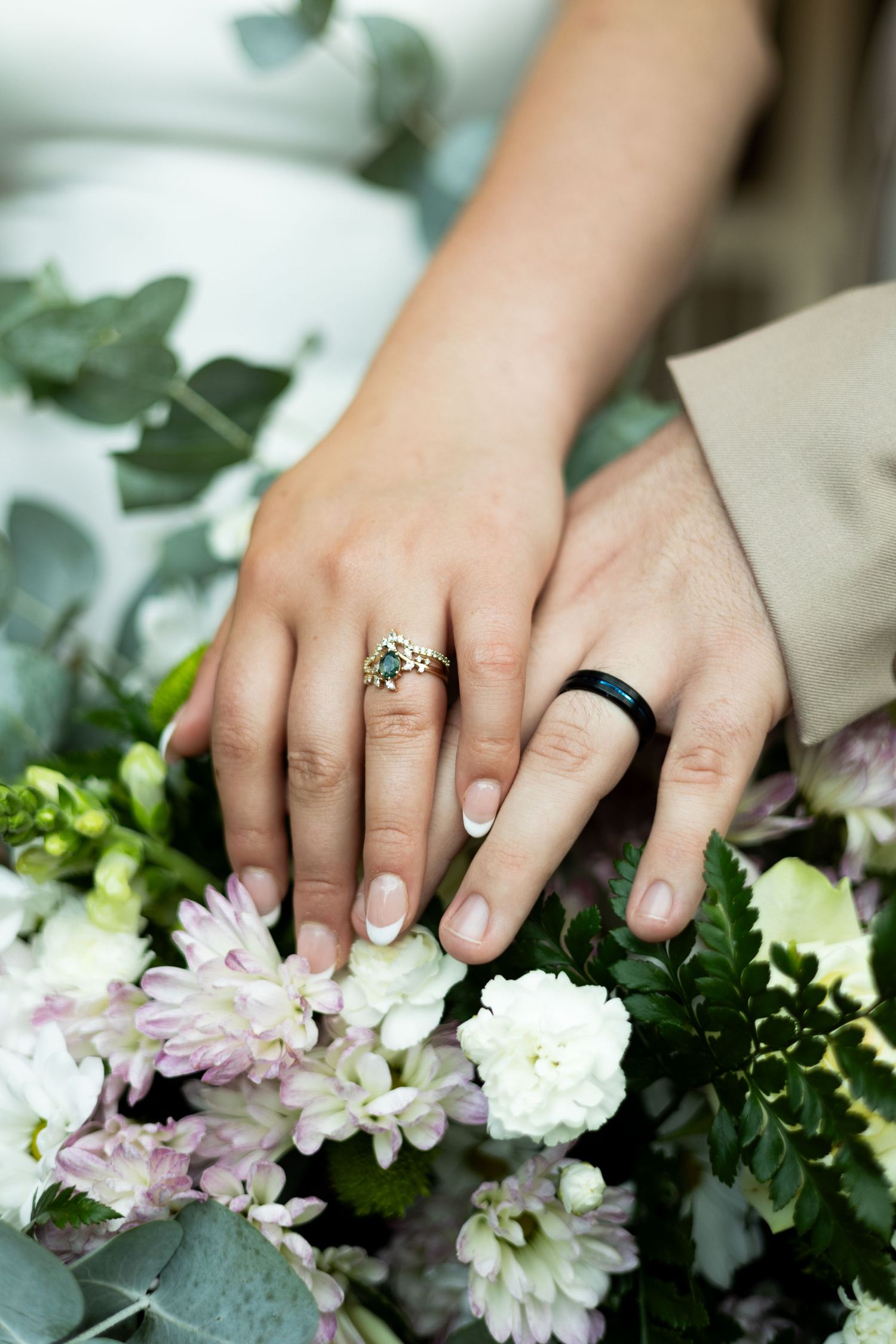 Wedding rings displayed on hands resting on a bouquet with white flowers and eucalyptus.