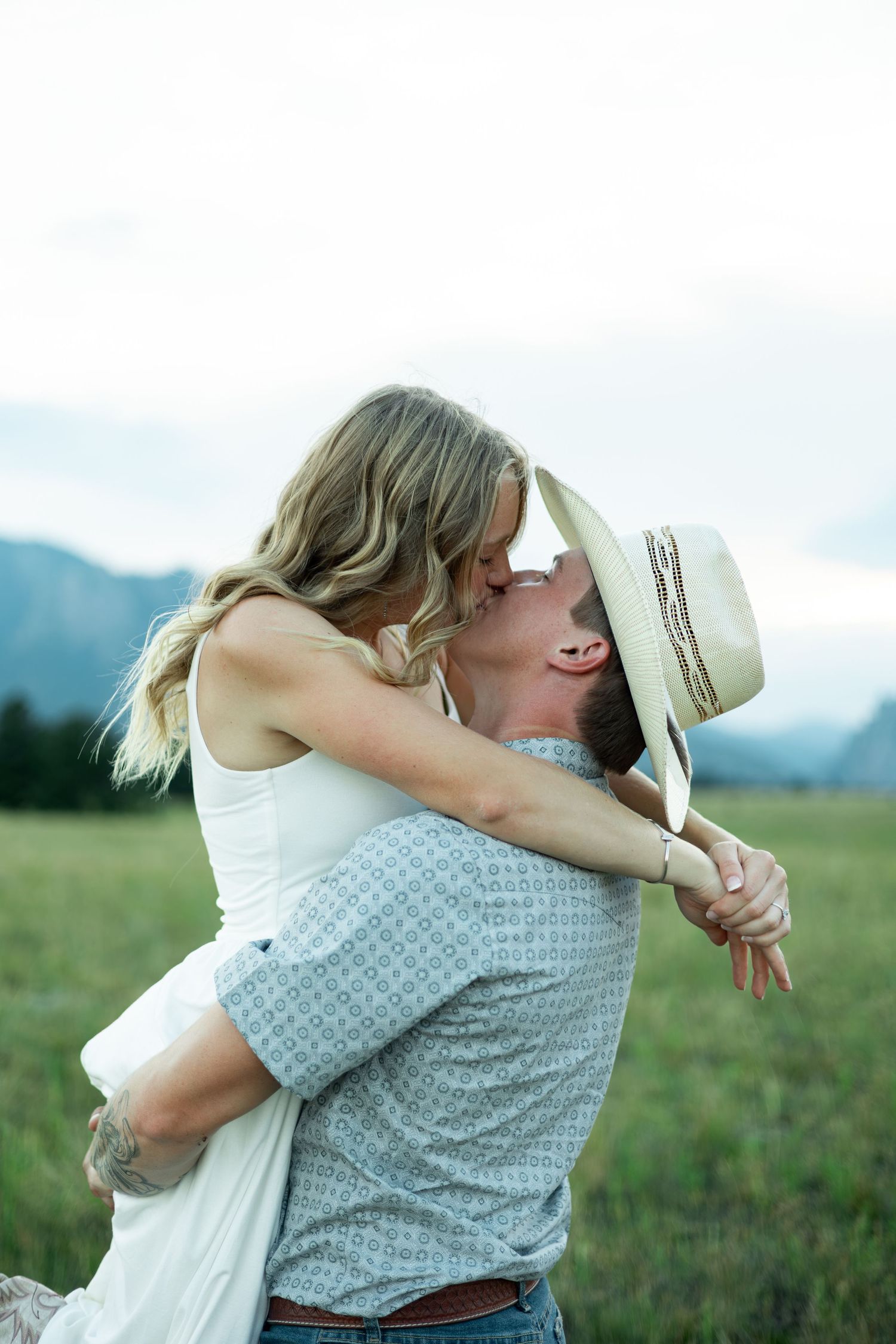 Romantic couple sharing a tender moment in a mountain meadow with a summer hat between them.