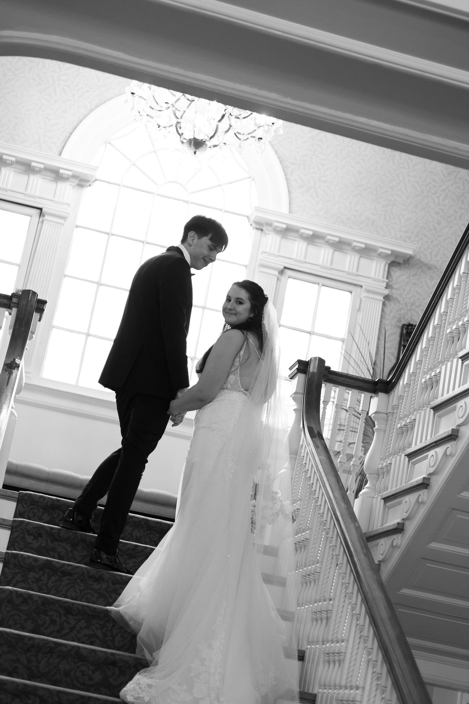A bride and groom share an intimate moment on an elegant white staircase with an arched entryway in black and white.