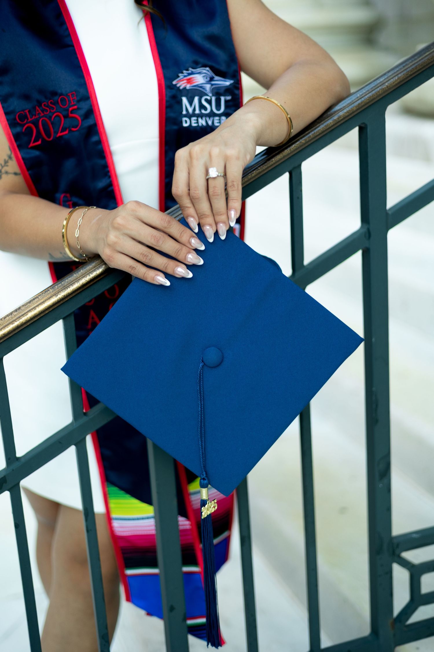 Graduate holding a blue MSU Dental graduation cap with rings and jewelry visible on their hands.