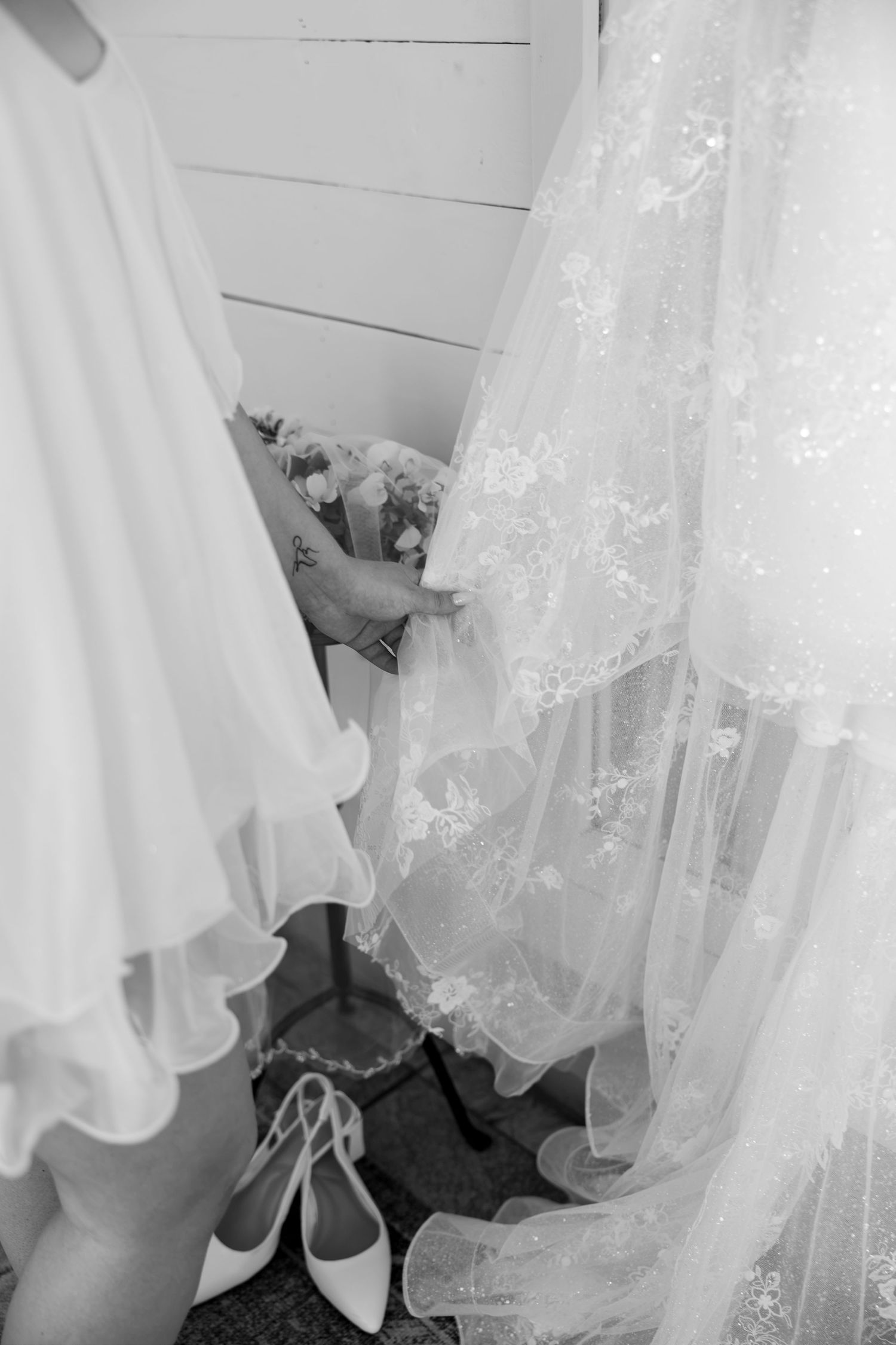 Black and white photo of wedding dress, veil, and bridal heels on floor during bridal preparations.