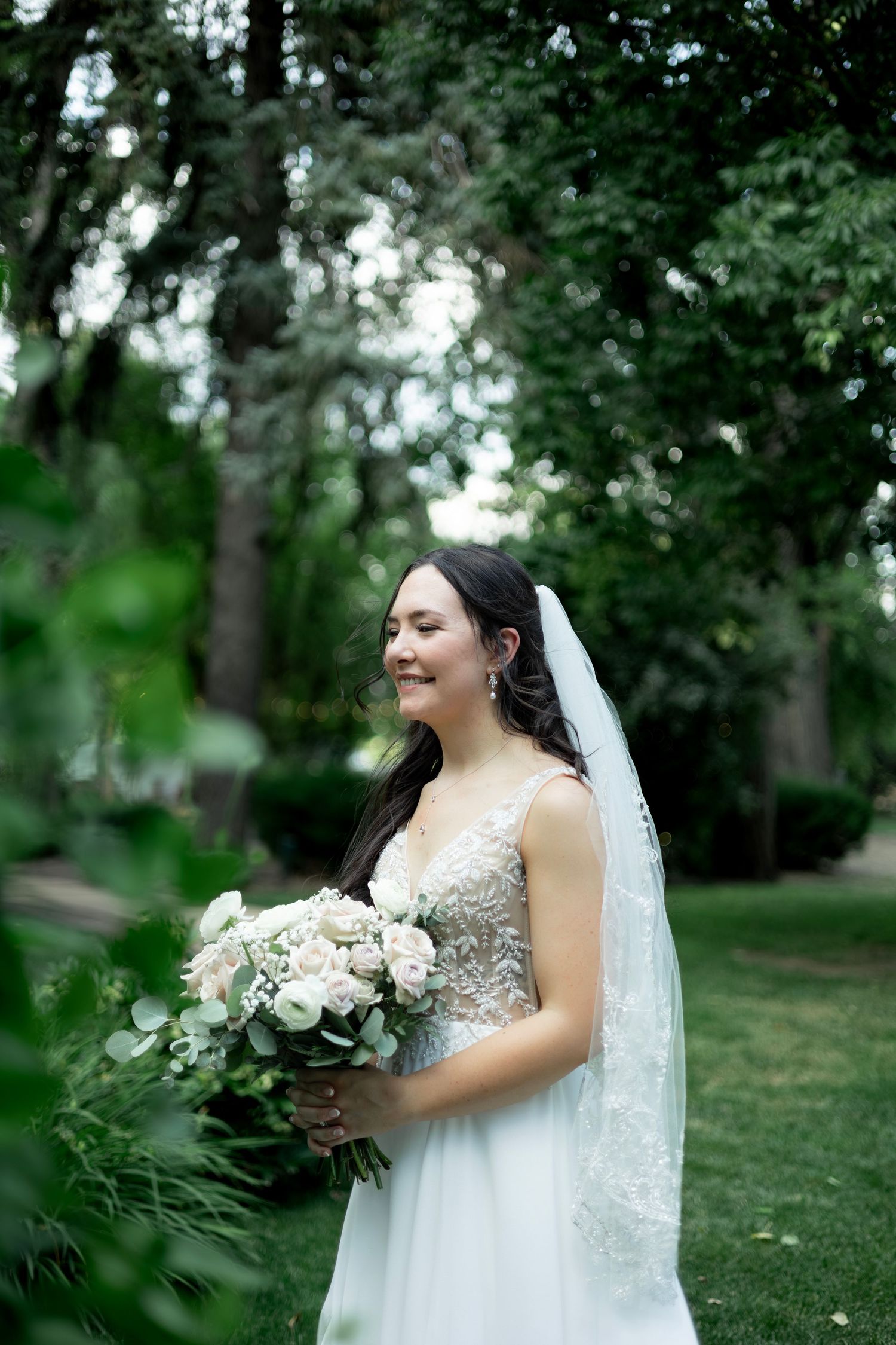 A joyful moment in a garden setting with a white floral bouquet and flowing veil.