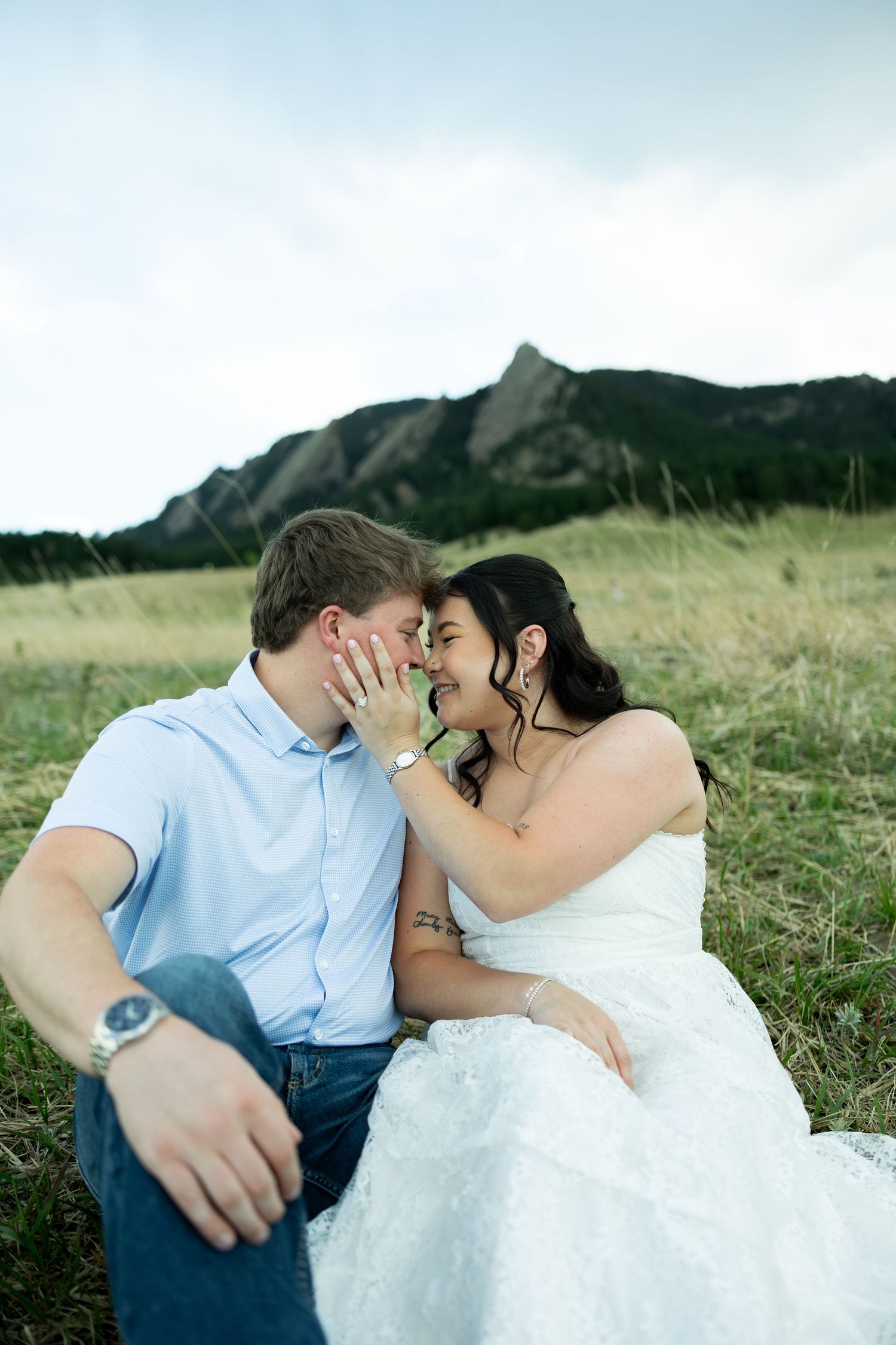 Bride and groom sit romantically in a grassy field with the Flatirons mountains of Boulder, Colorado in the background.