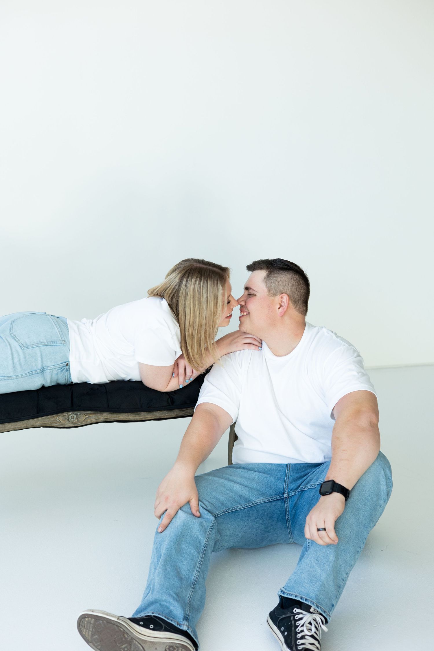A couple in casual white t-shirts and jeans sharing an intimate moment in a bright minimalist setting.