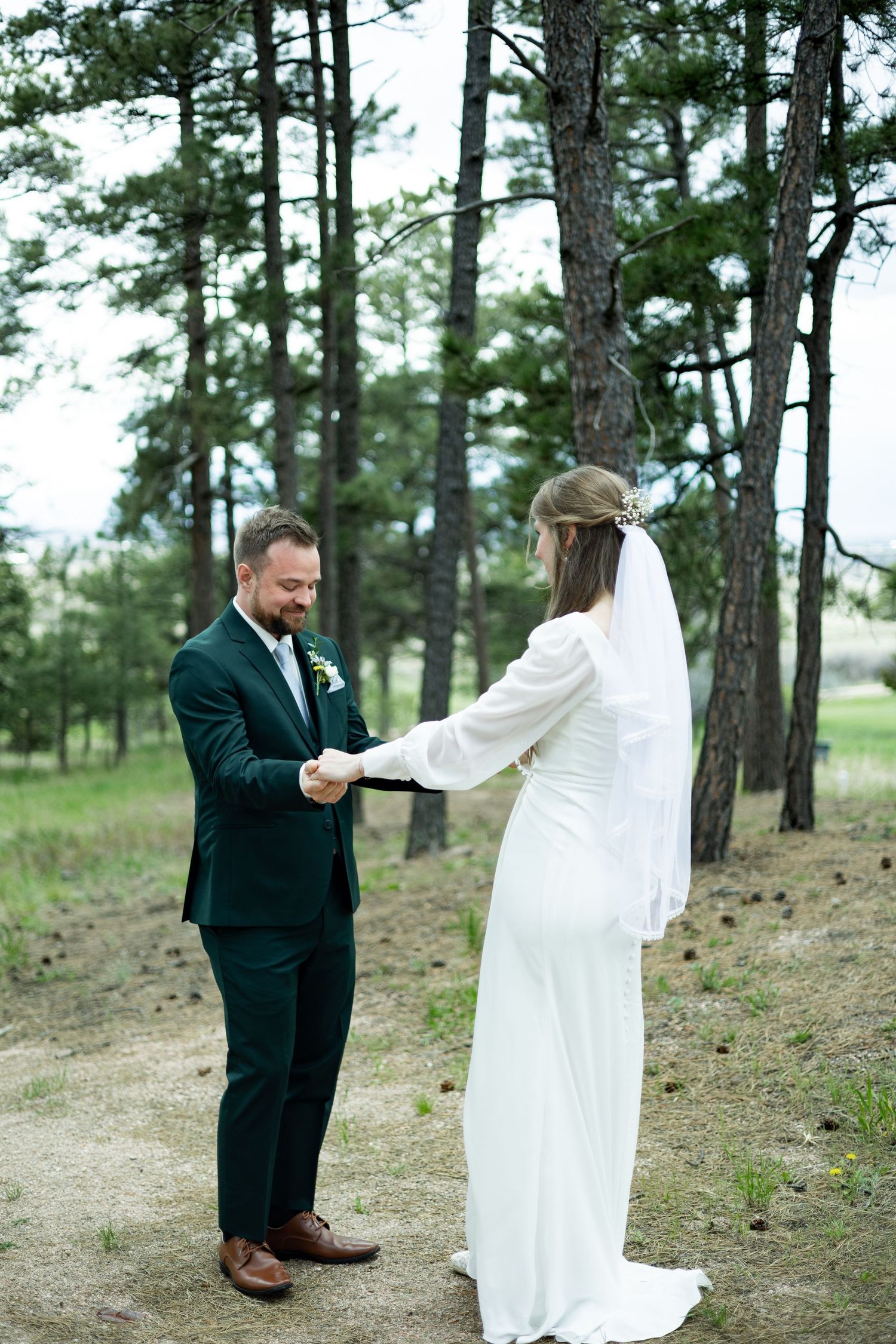Wedding couple shares an intimate moment exchanging vows in a pine forest setting in elegant attire.