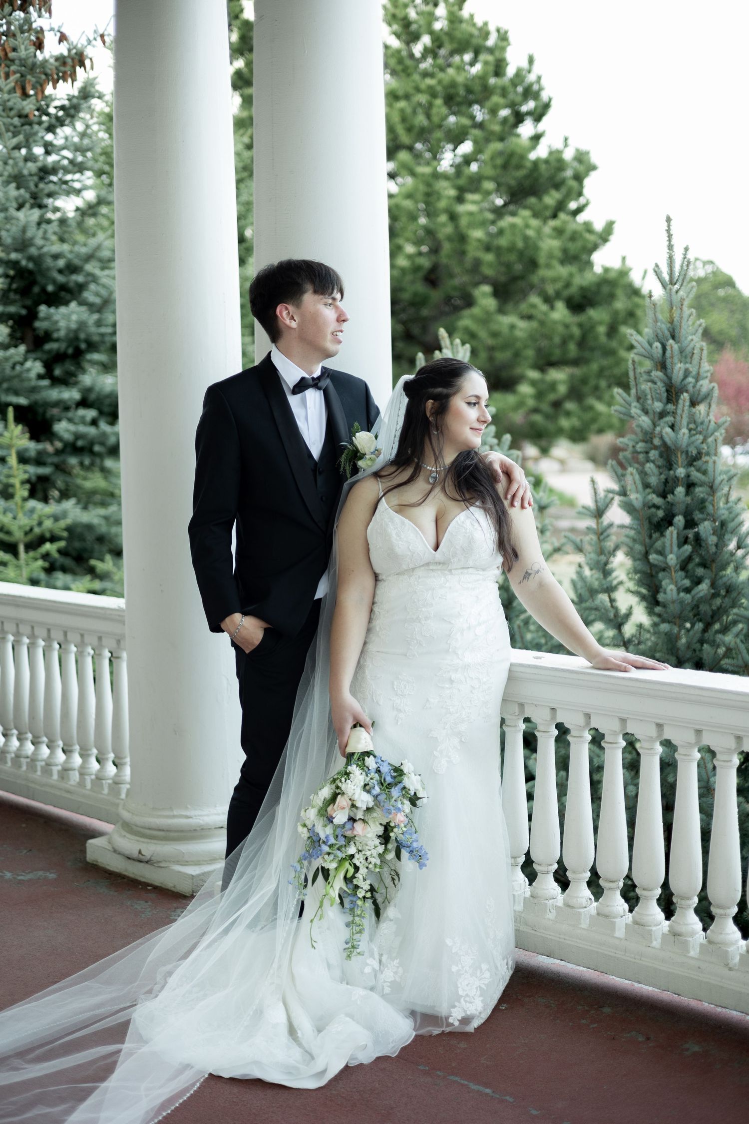 A couple poses on a columned veranda with white balustrades during their wedding photoshoot.