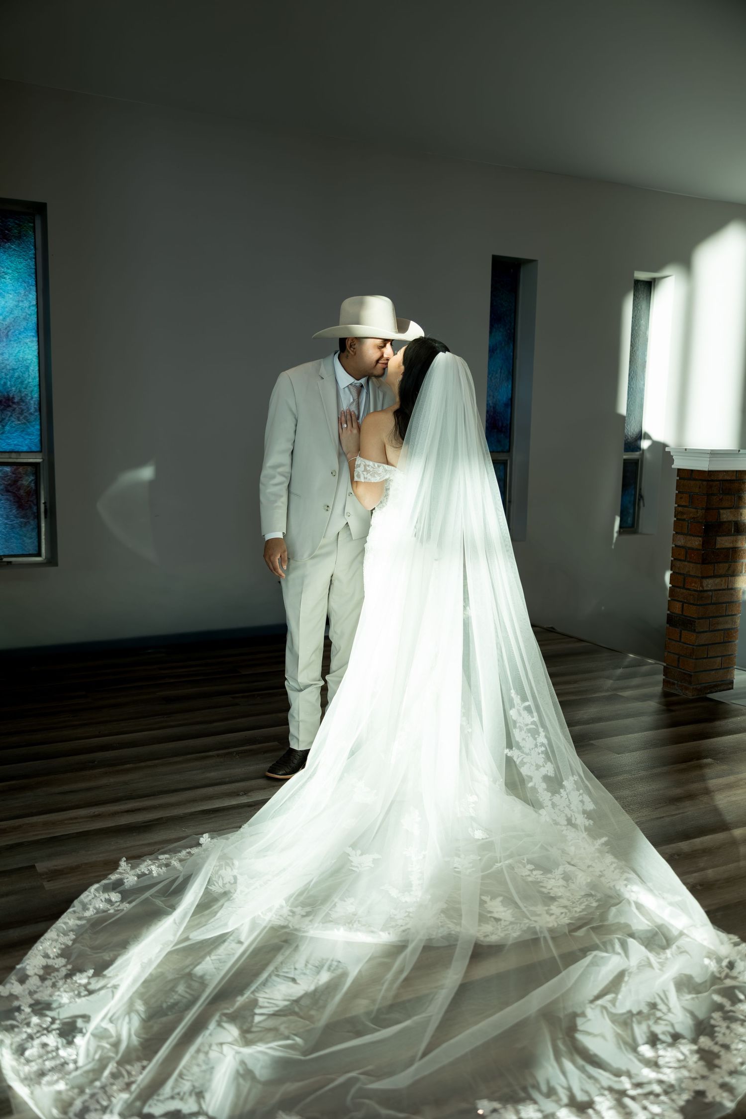 A dramatic wedding scene with flowing cathedral veil and natural light streaming through windows.