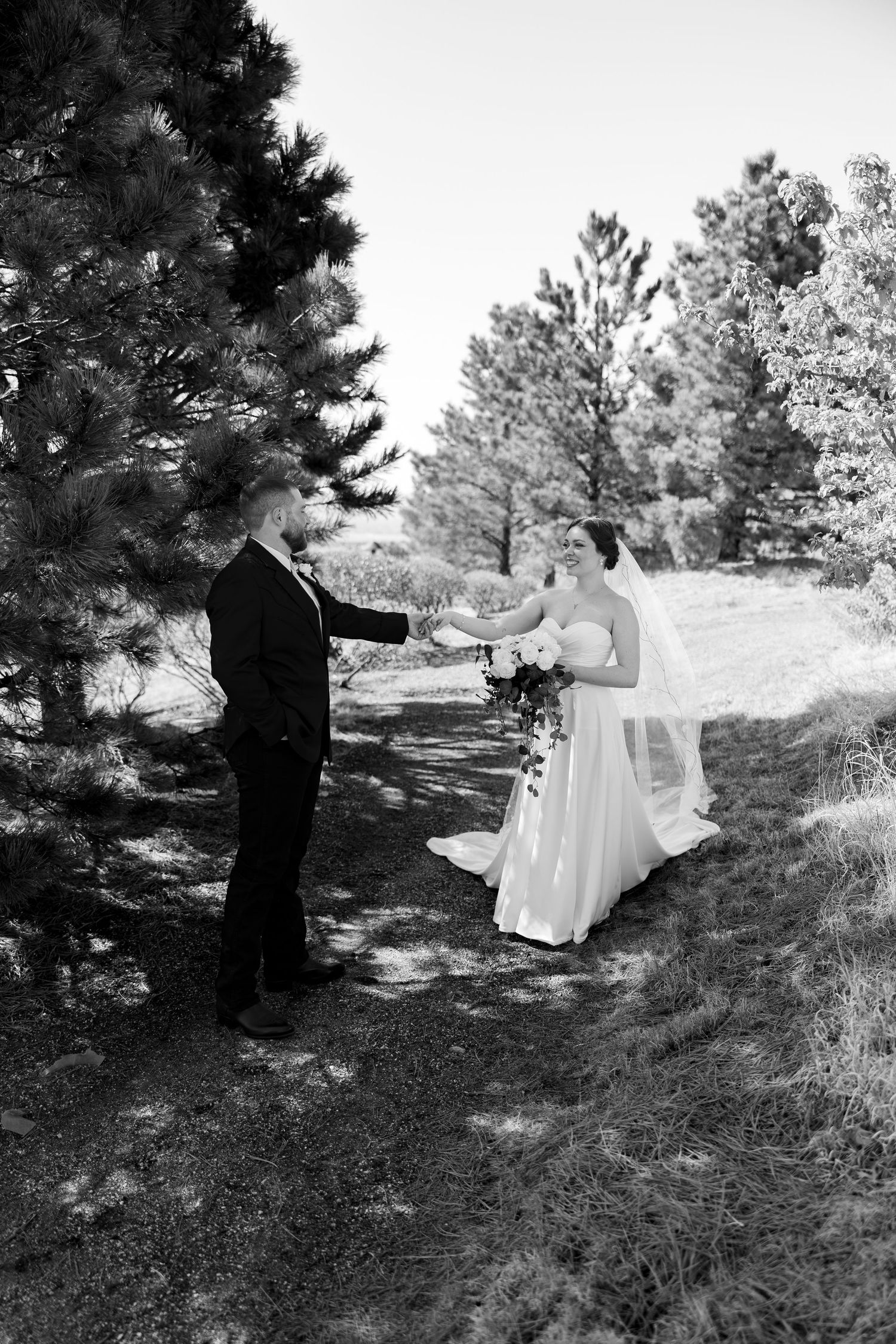 Black and white photo of bride and groom holding hands on a forest path during their wedding first look.