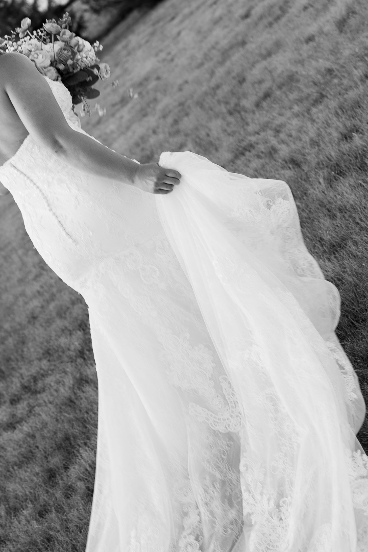 Black and white photo of a bride in a lace wedding gown holding a bouquet, with her dress flowing gracefully.