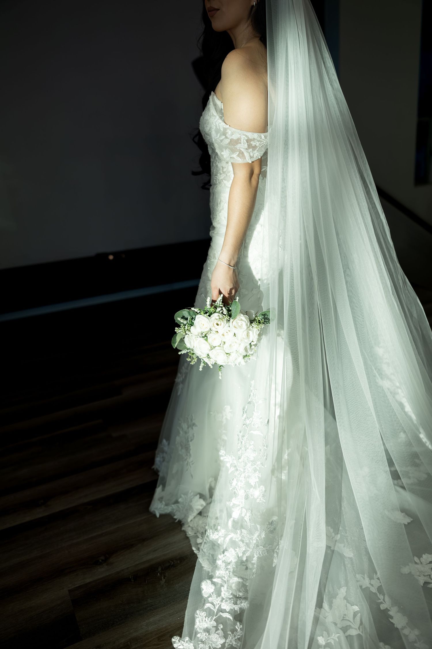 A bride in an off-shoulder wedding gown holds a cascading white bouquet with a flowing cathedral veil.