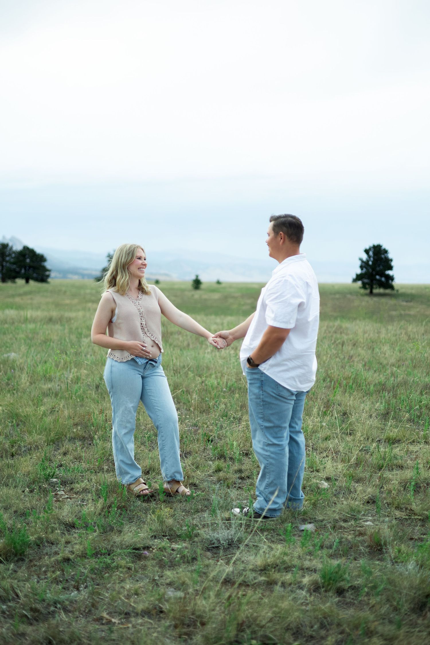 A couple stands together in a grassy meadow on a sunny day sharing a tender moment in casual attire.