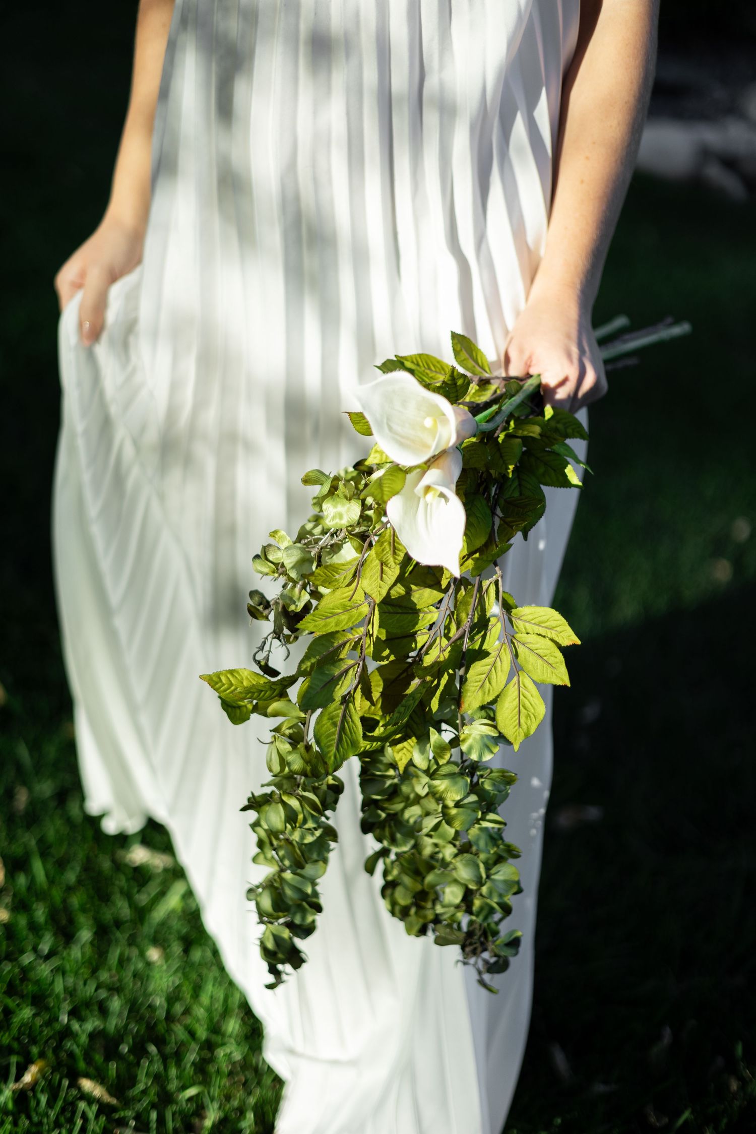 A series of images showing a white dress against a dark background with green foliage being held in frame.